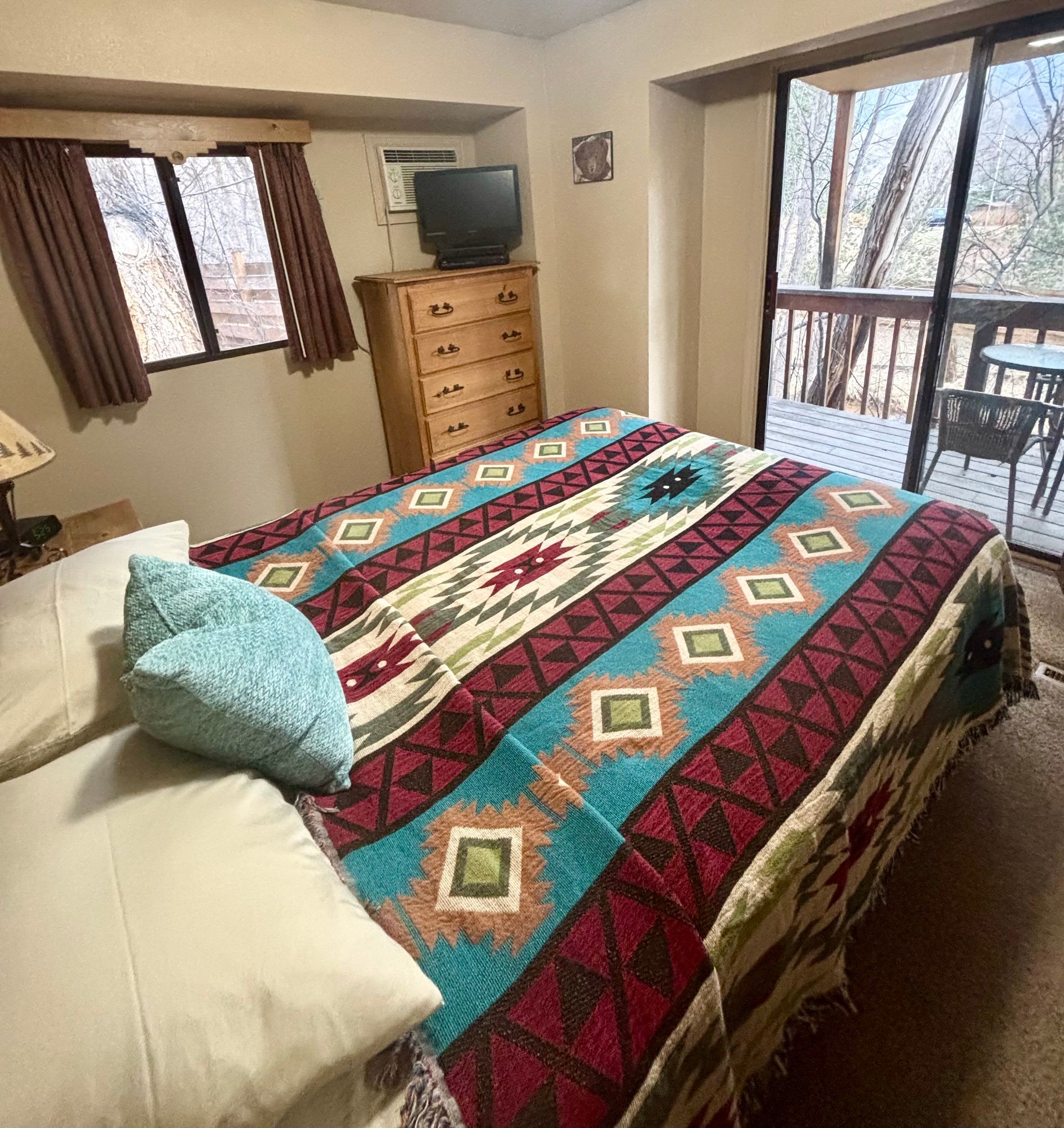 Bedroom with bed, dresser, TV, window, and balcony access. Southwestern-style bedspread; brown curtains.