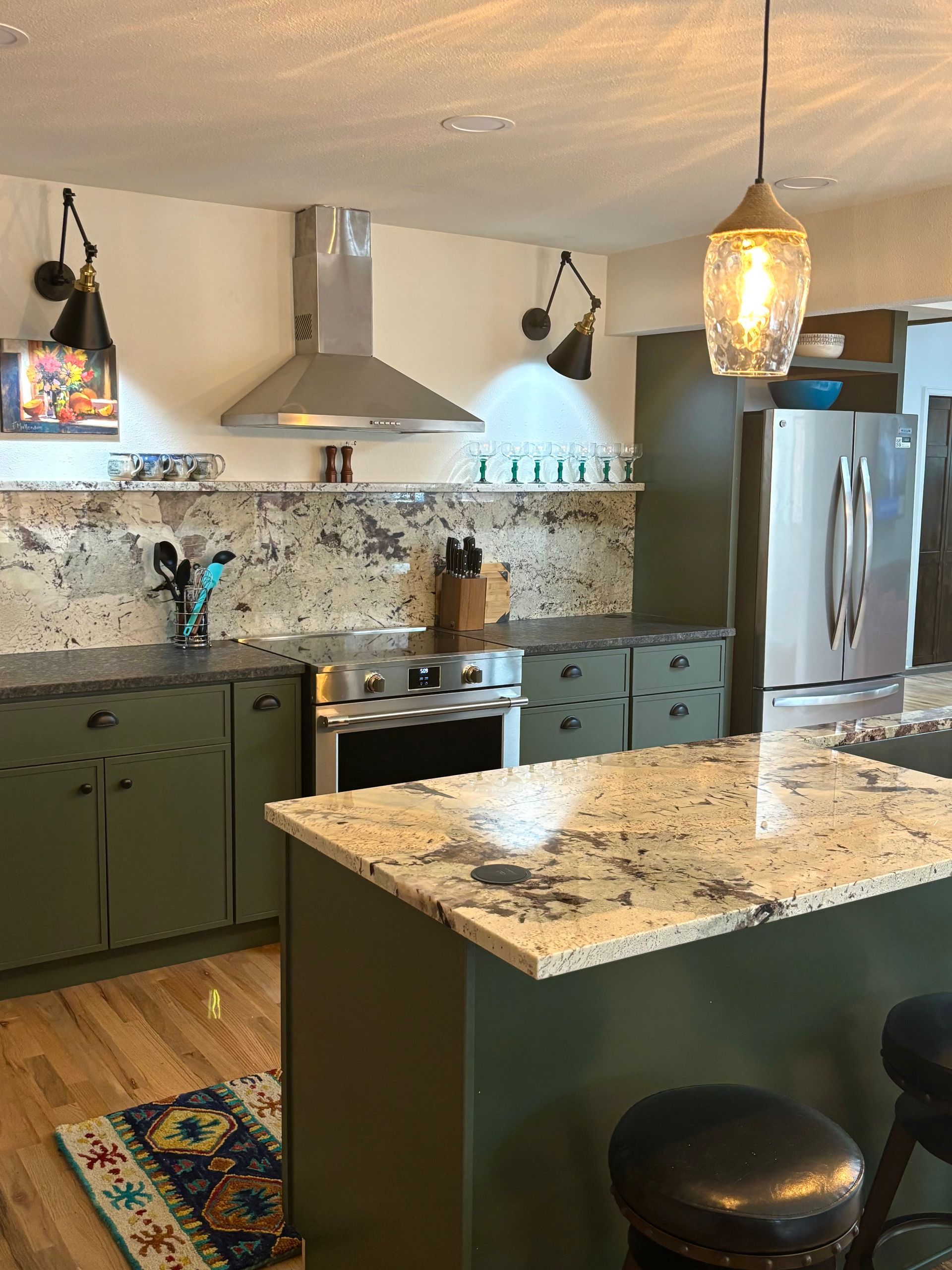Green kitchen with stainless steel appliances, granite countertops, and decorative lighting.