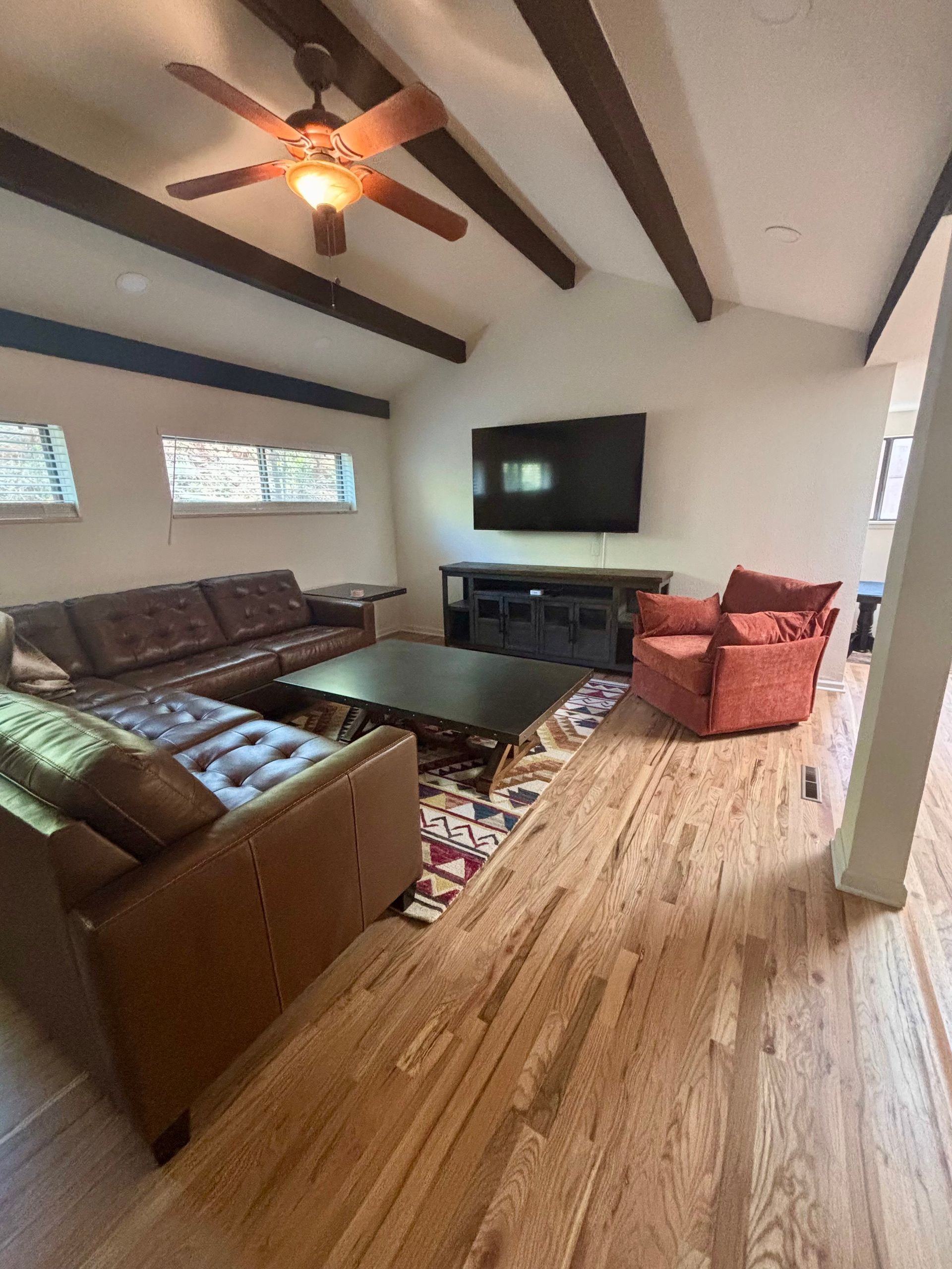 Living room with leather sofa, TV, and wood ceiling beams.