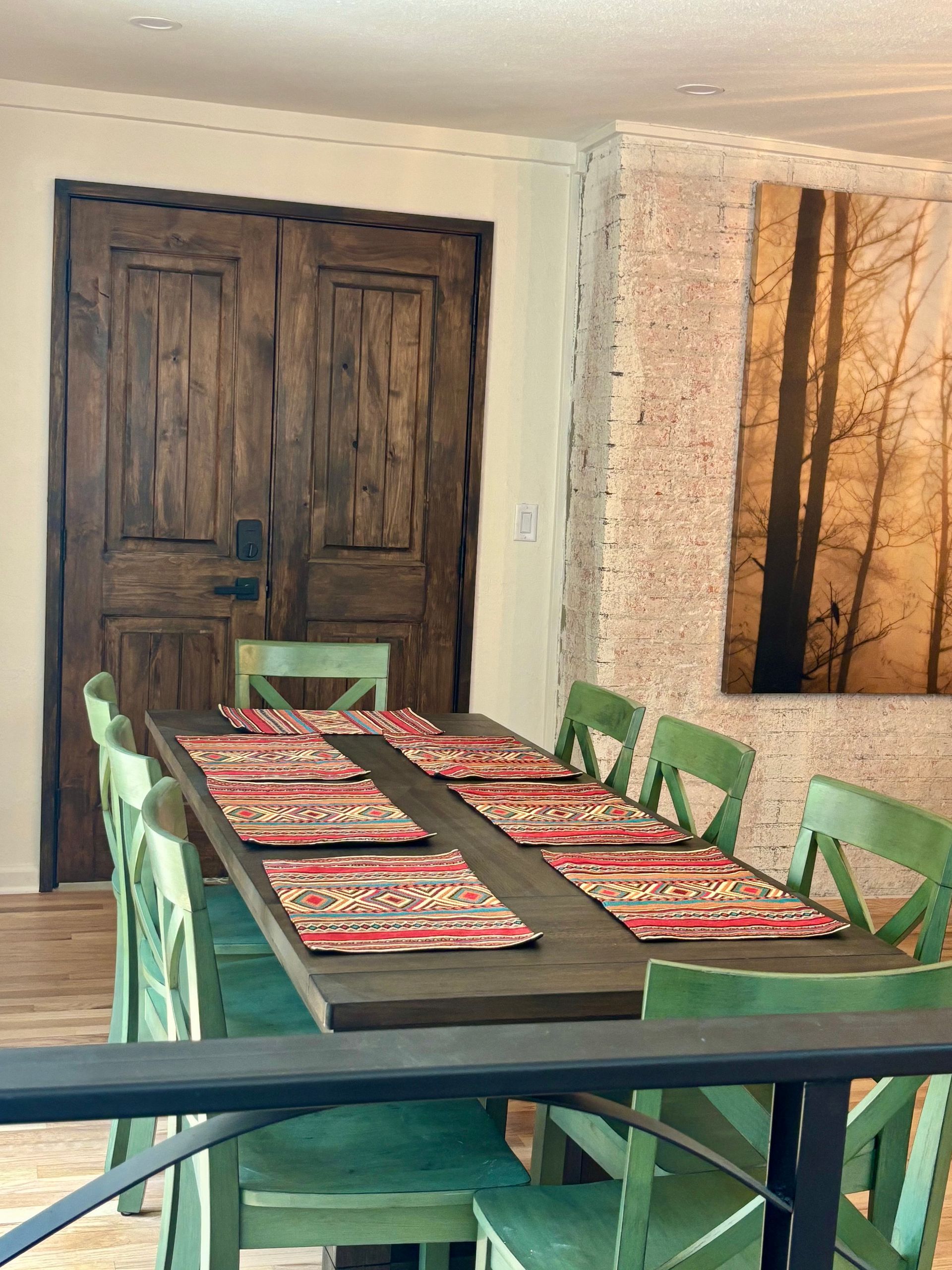 Dining room with green chairs, long wooden table set for meal, and rustic wooden door.