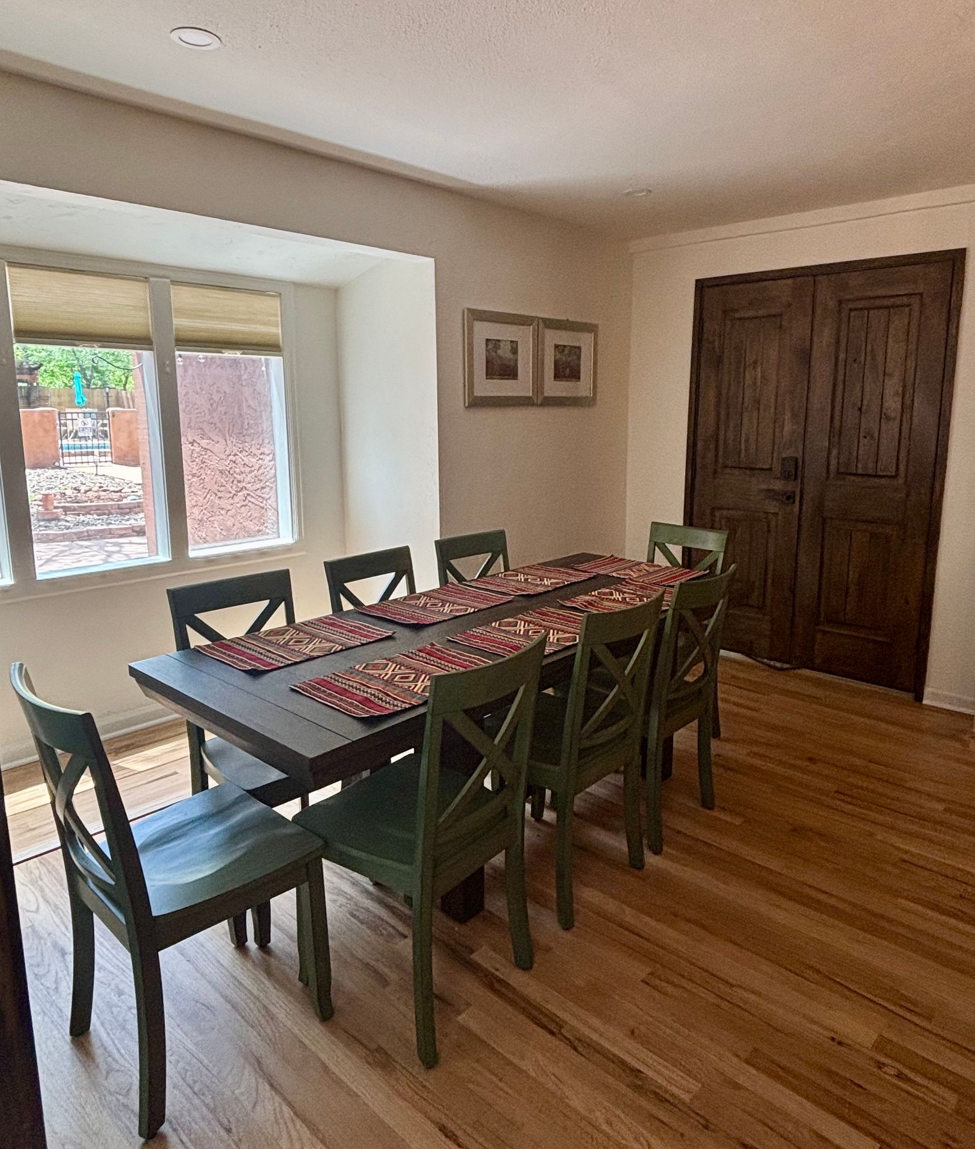 Dining room with dark table, green chairs, and wooden floor. Window and wood double doors visible.