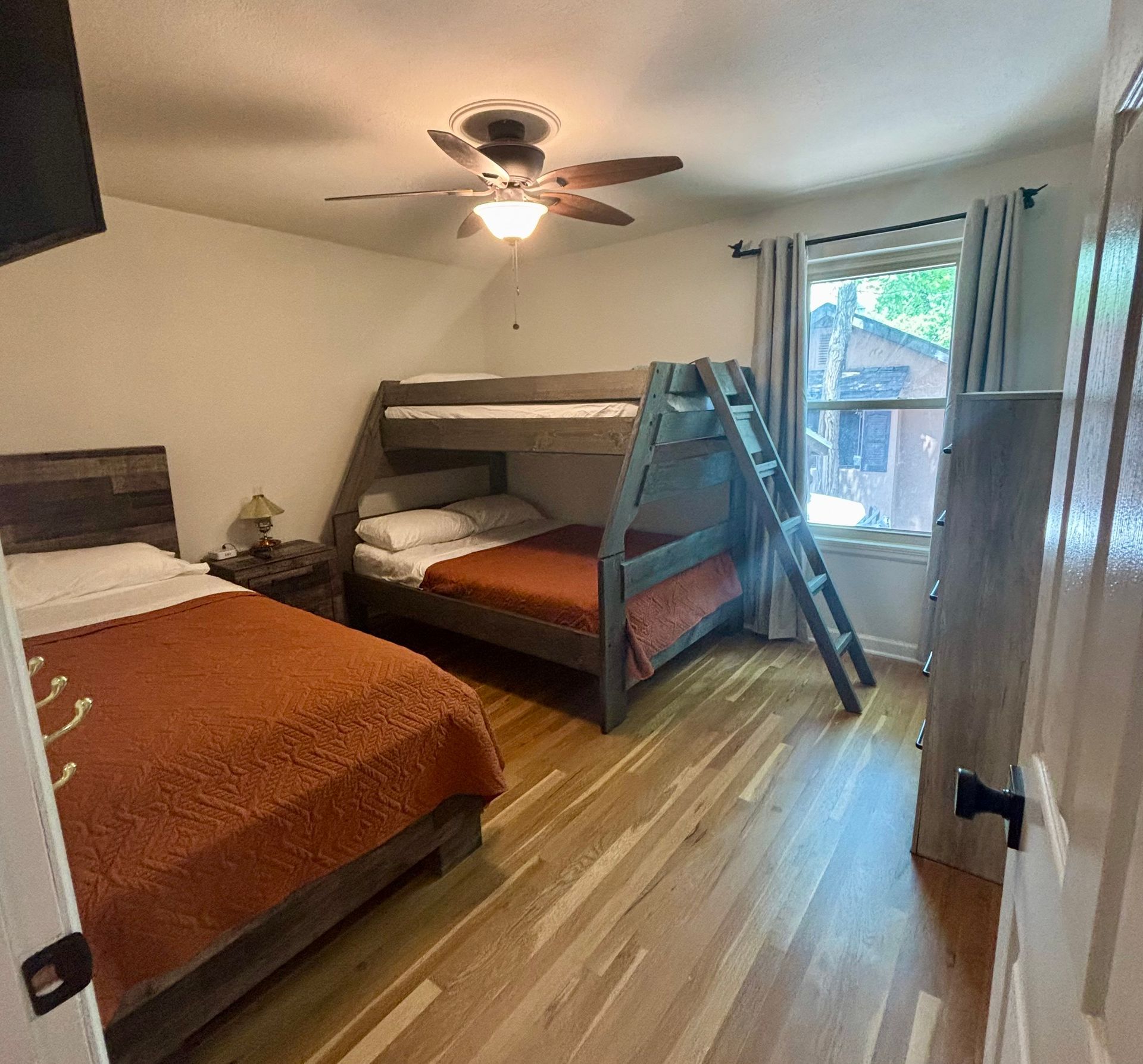 Bedroom with bunk bed, double bed, wooden floor. Window with grey curtains.
