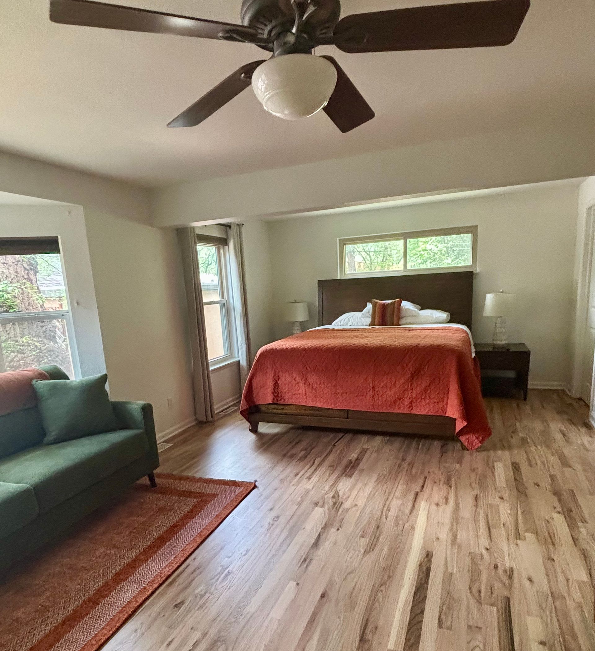 Bedroom with bed, green couch, red rug, wooden floor, and ceiling fan.