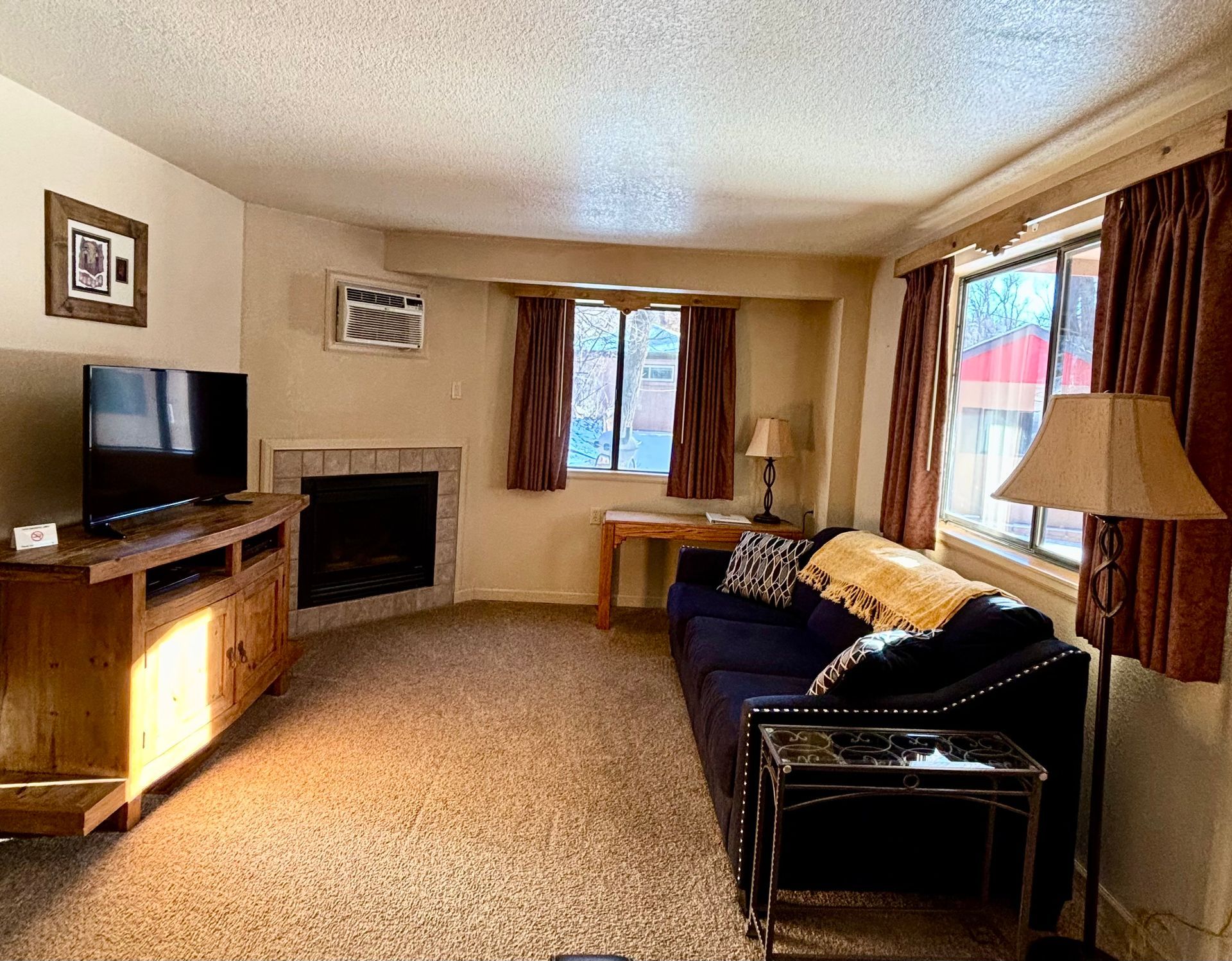 Living room with a fireplace, TV, sofa, and window with brown curtains.