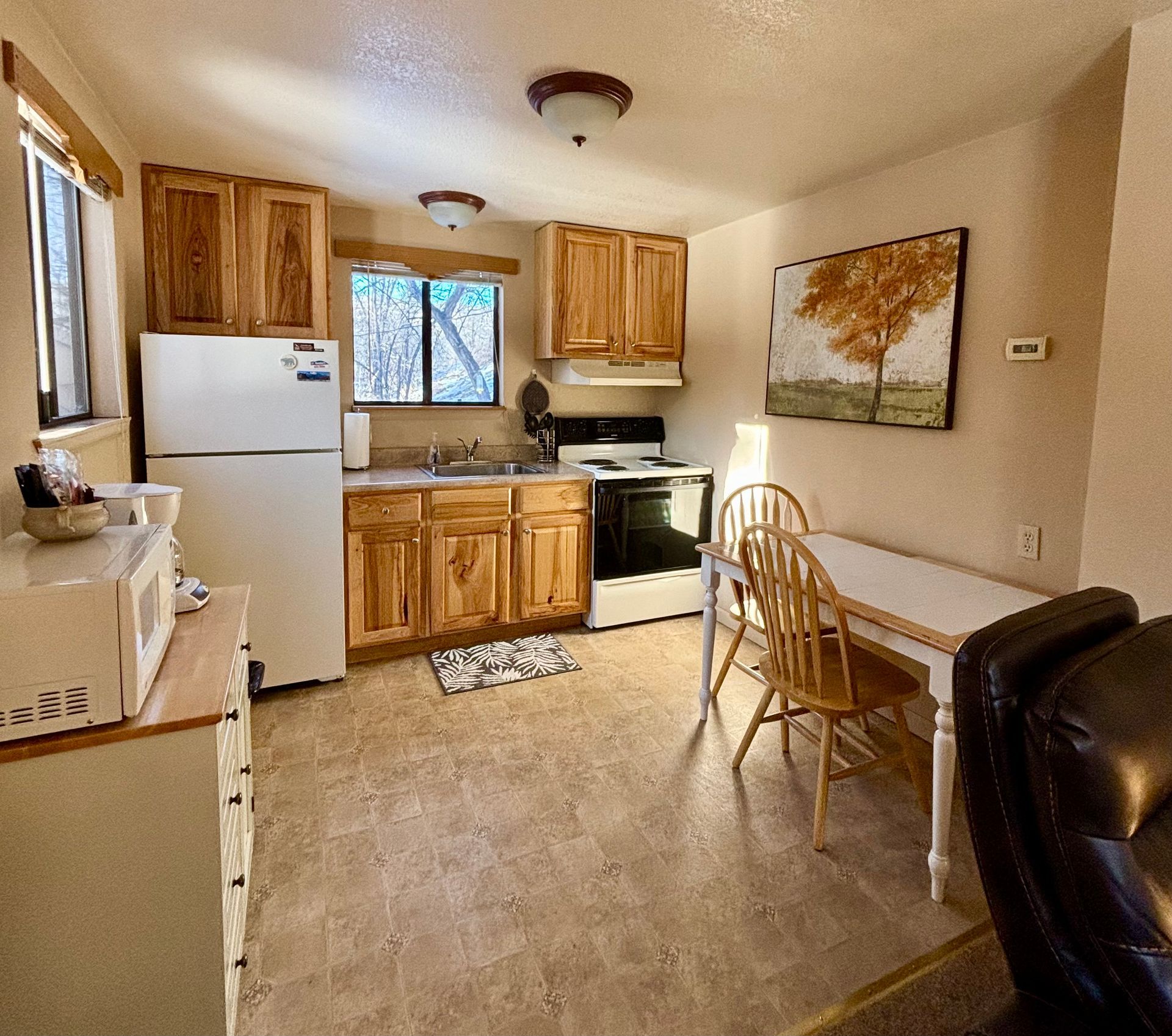 Small kitchen with wooden cabinets, white appliances, and a table with two chairs.