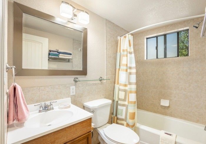 Bathroom with beige tile, white sink and toilet, shower with curtain, and window.