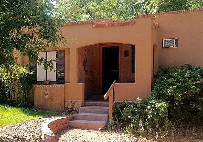 Tan adobe home with arched entrance, steps, and greenery.