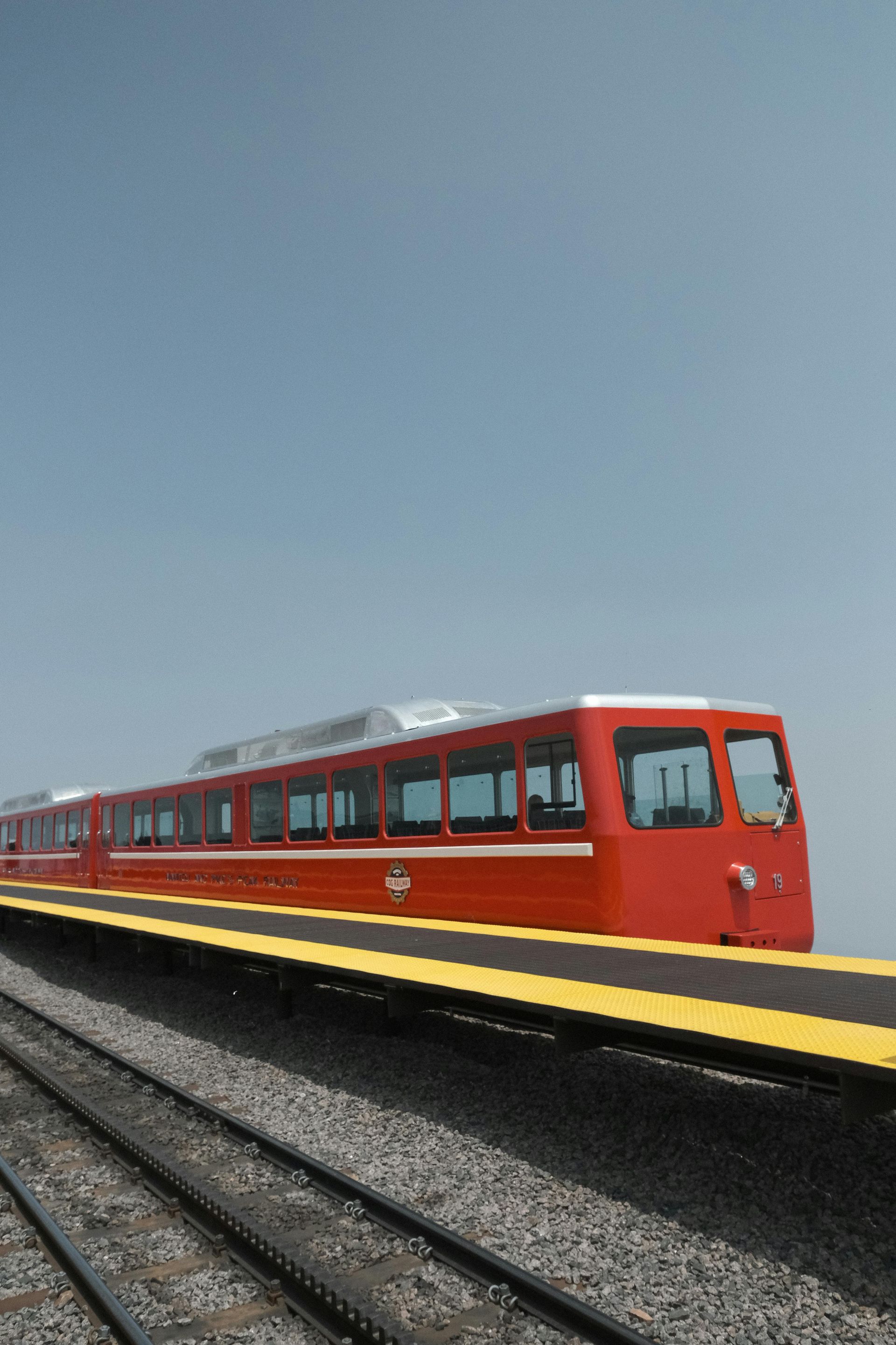 Red train on a yellow platform against a hazy sky. Tracks in foreground.
