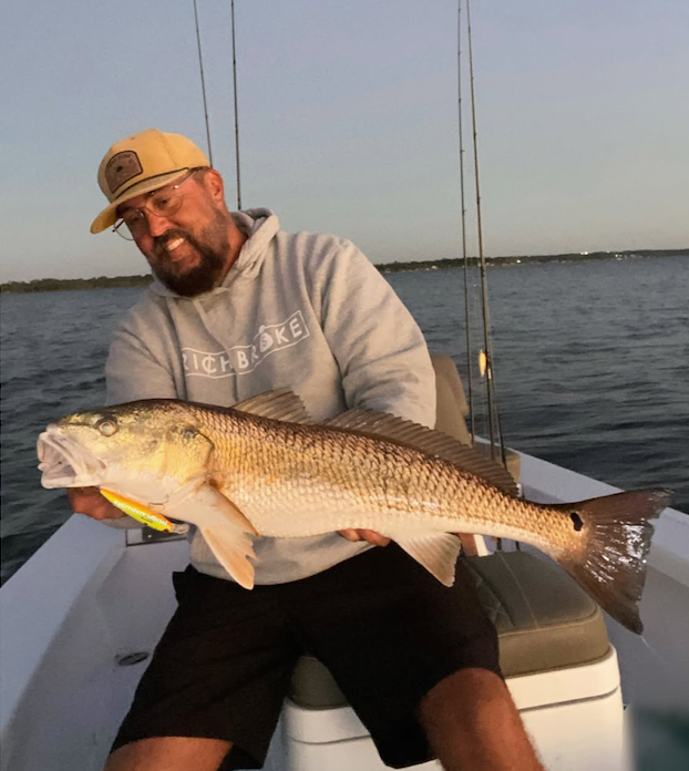 A customer holding a redfish aboard a Legendary skiff at dusk