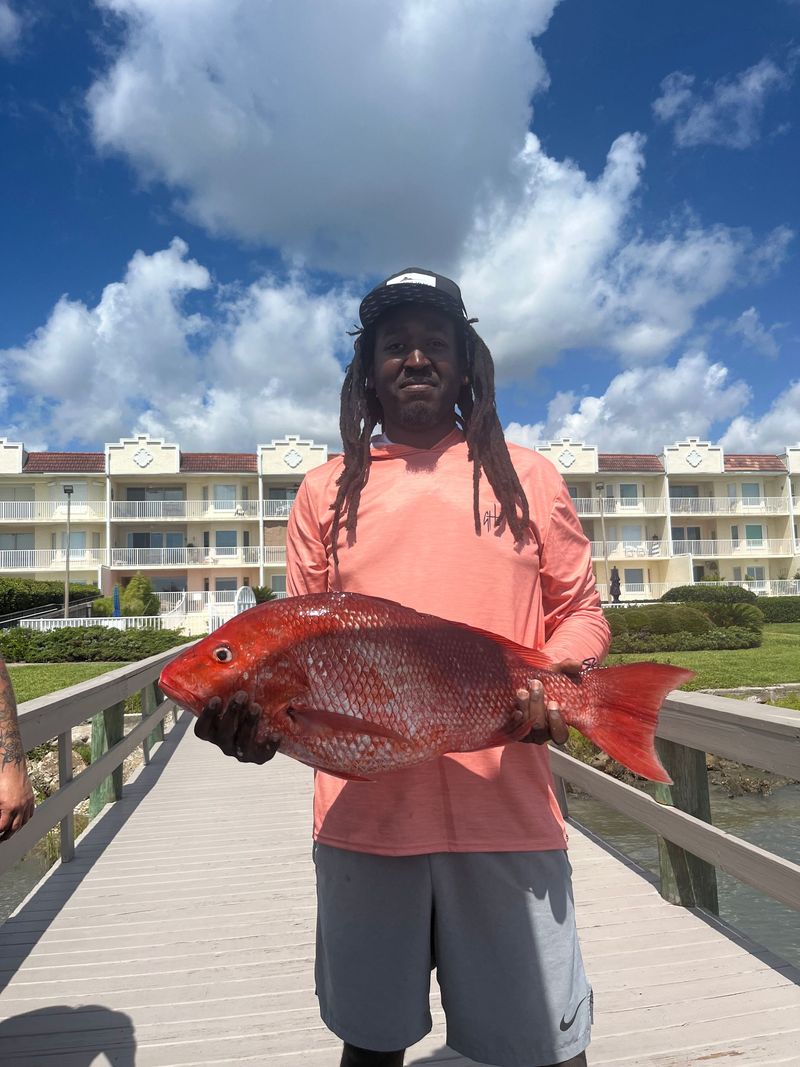 An angler holding a red snapper on a dock