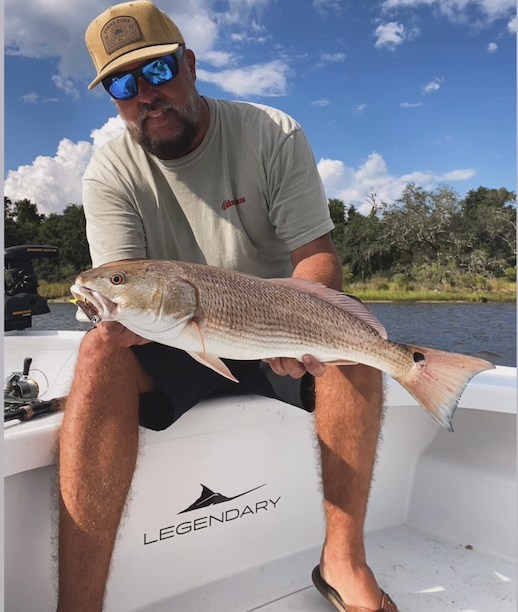 A customer holding a redfish on the casting deck of a Legendary skiff