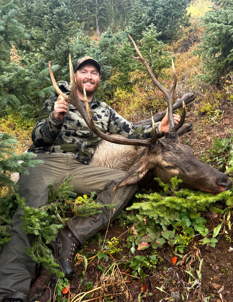 A hunter smiling beside an elk in the woods