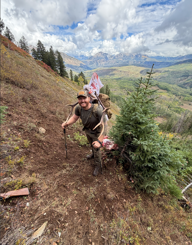 A hunter packing out elk antlers on a mountain trail