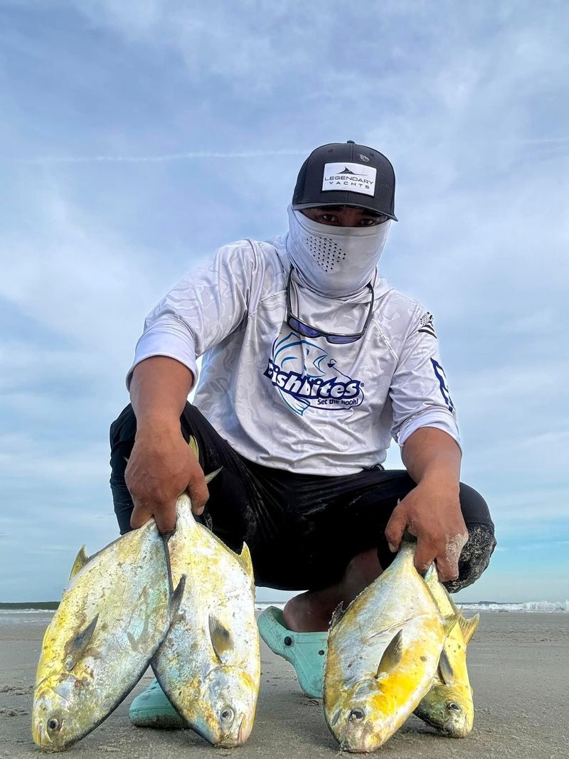 An angler crouching on the beach with a catch of pompano