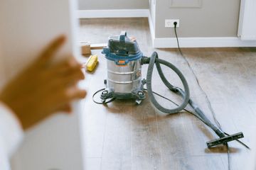 Shop vacuum and hose on a wooden floor in a sparsely furnished room