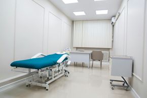 Empty examination room with teal treatment table, desk, chair, and white walls