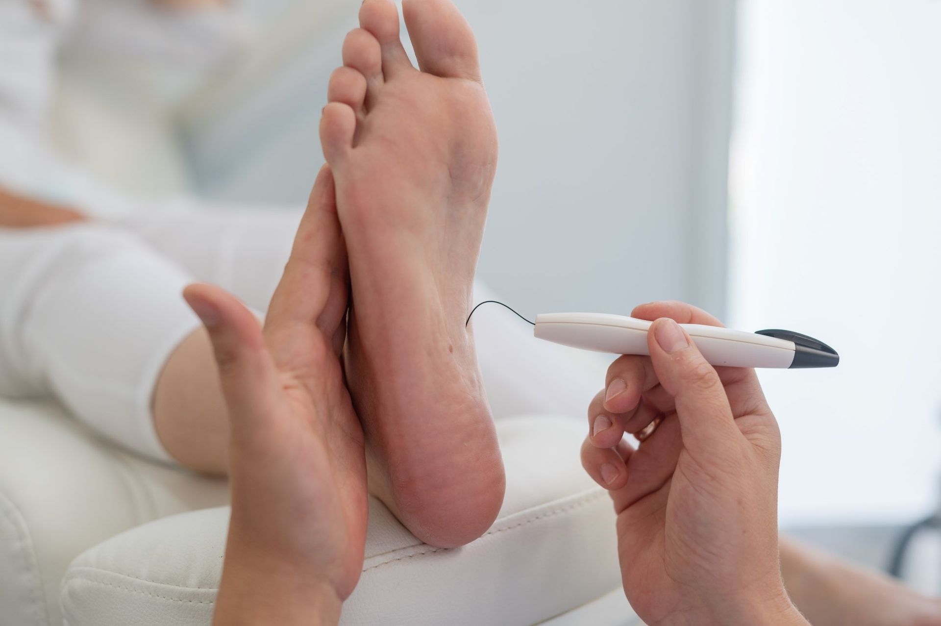 A person is holding a tool over a person's foot. — Maitland Central Podiatry in Maitland NSW