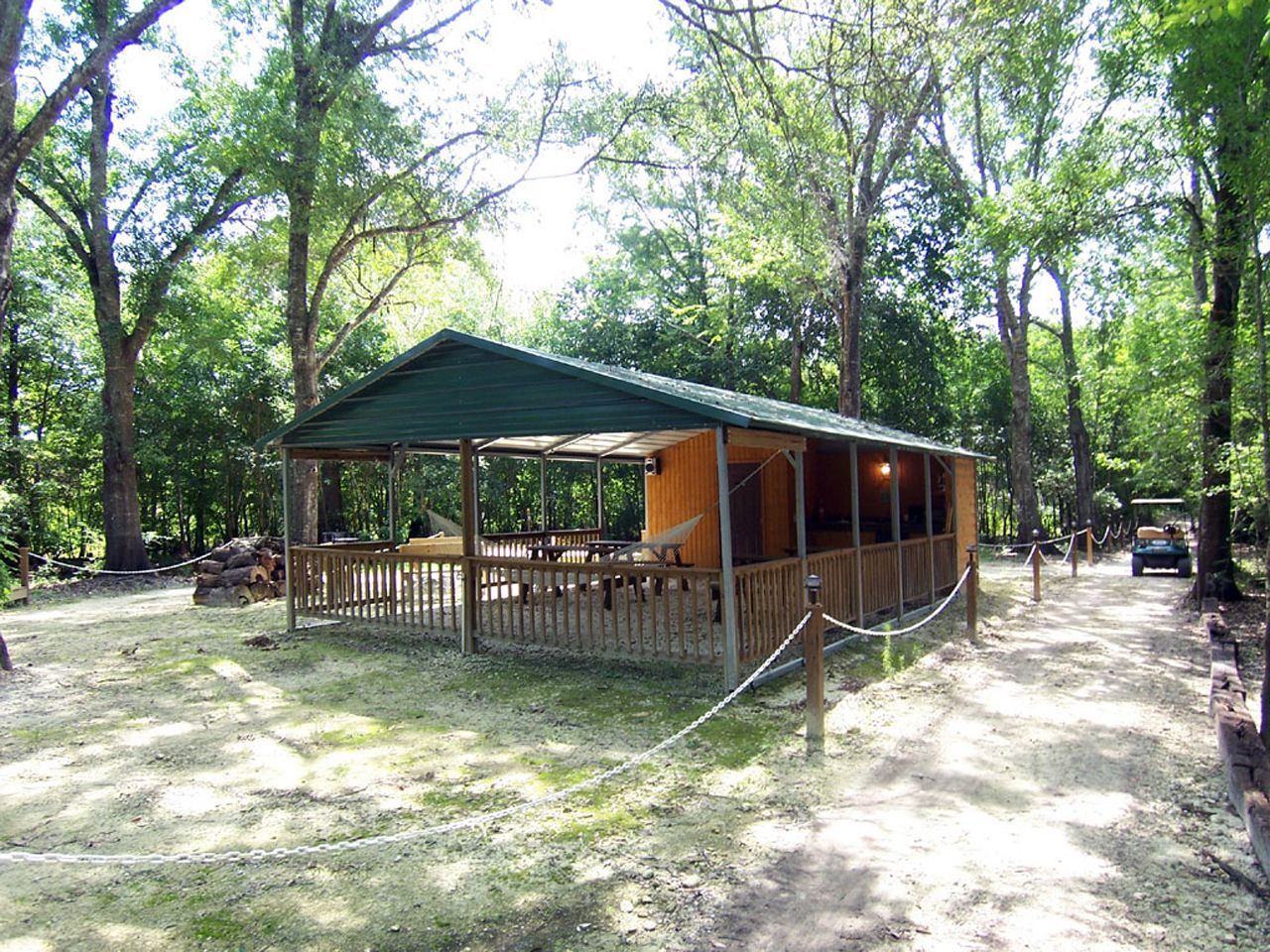 a pavilion with a green roof and a wooden deck in the middle of a forest .