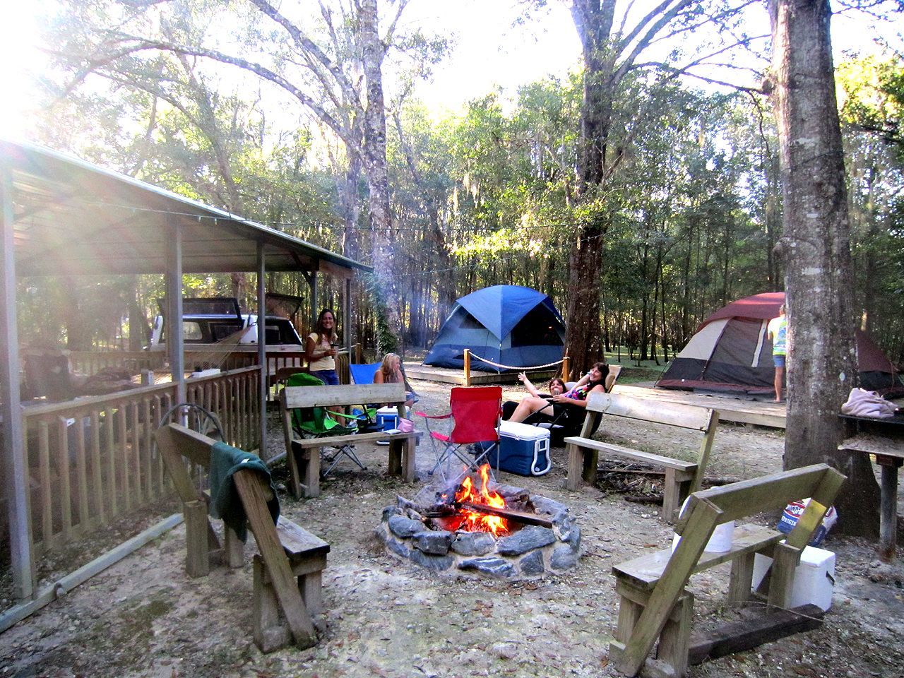 a group of people are sitting around a fire pit in a campground .