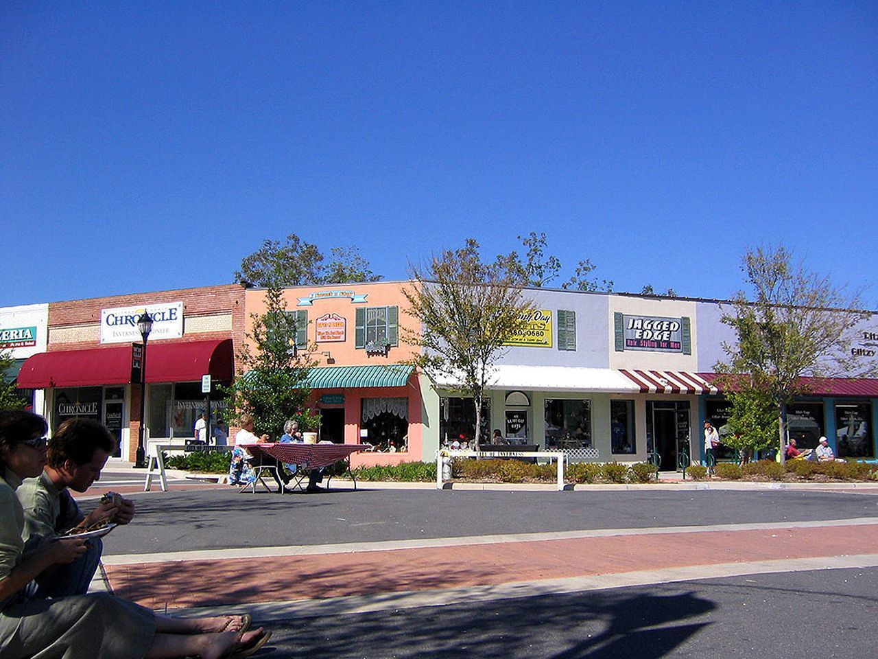 a group of people are sitting on the sidewalk in front of a row of stores including one that says ' dreams '