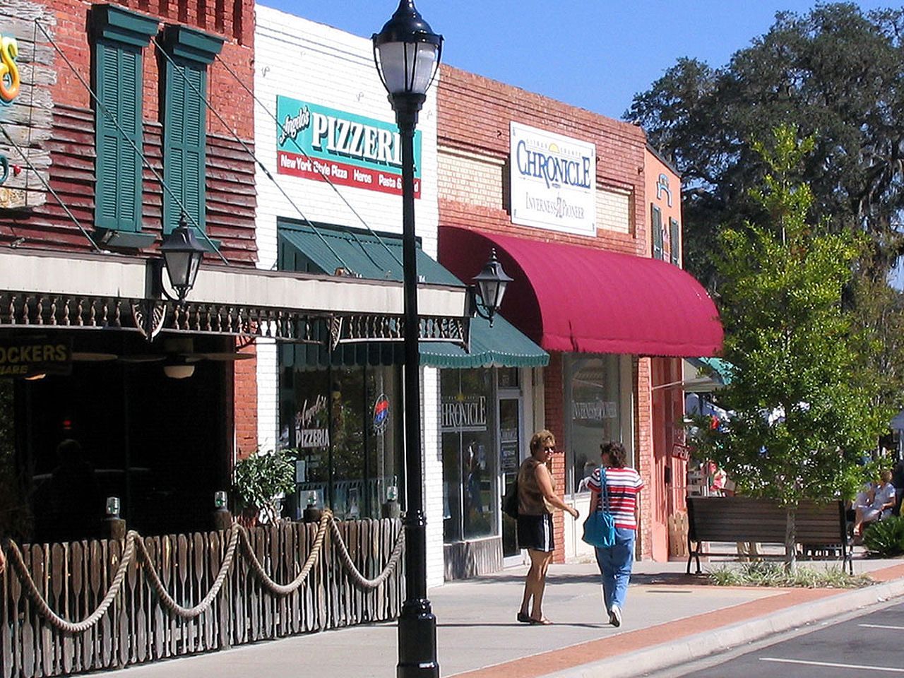 a woman walks down a sidewalk in front of a pizza hut