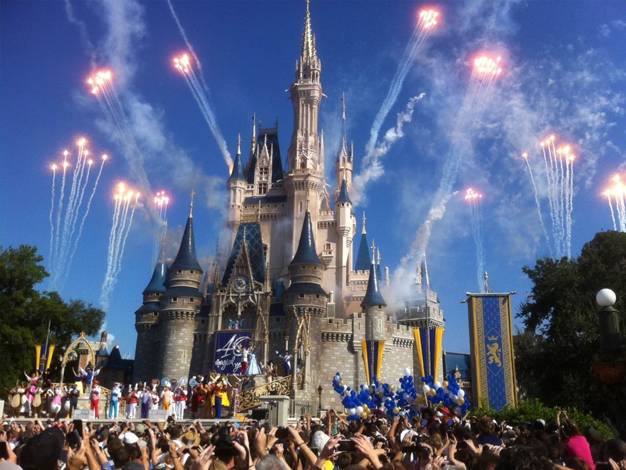 a crowd of people are gathered in front of a castle with fireworks going off