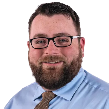 A man with a beard and glasses is wearing a blue shirt and tie.