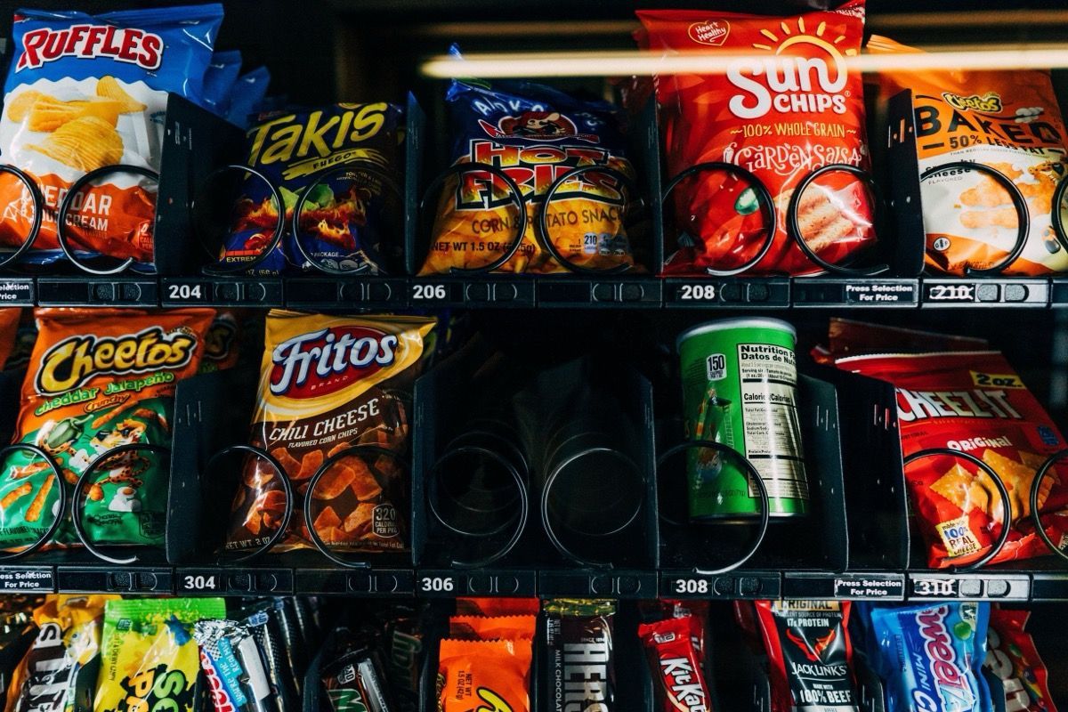 Snack shelves stocked with colorful chips, crackers, and canned drinks in a convenience store.