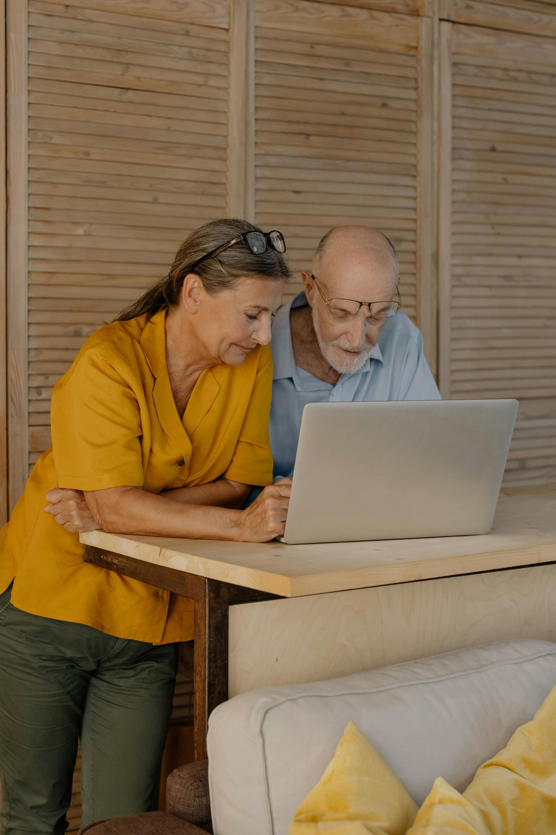 A man and a woman are sitting at a table with a laptop writing notes in a notebook.