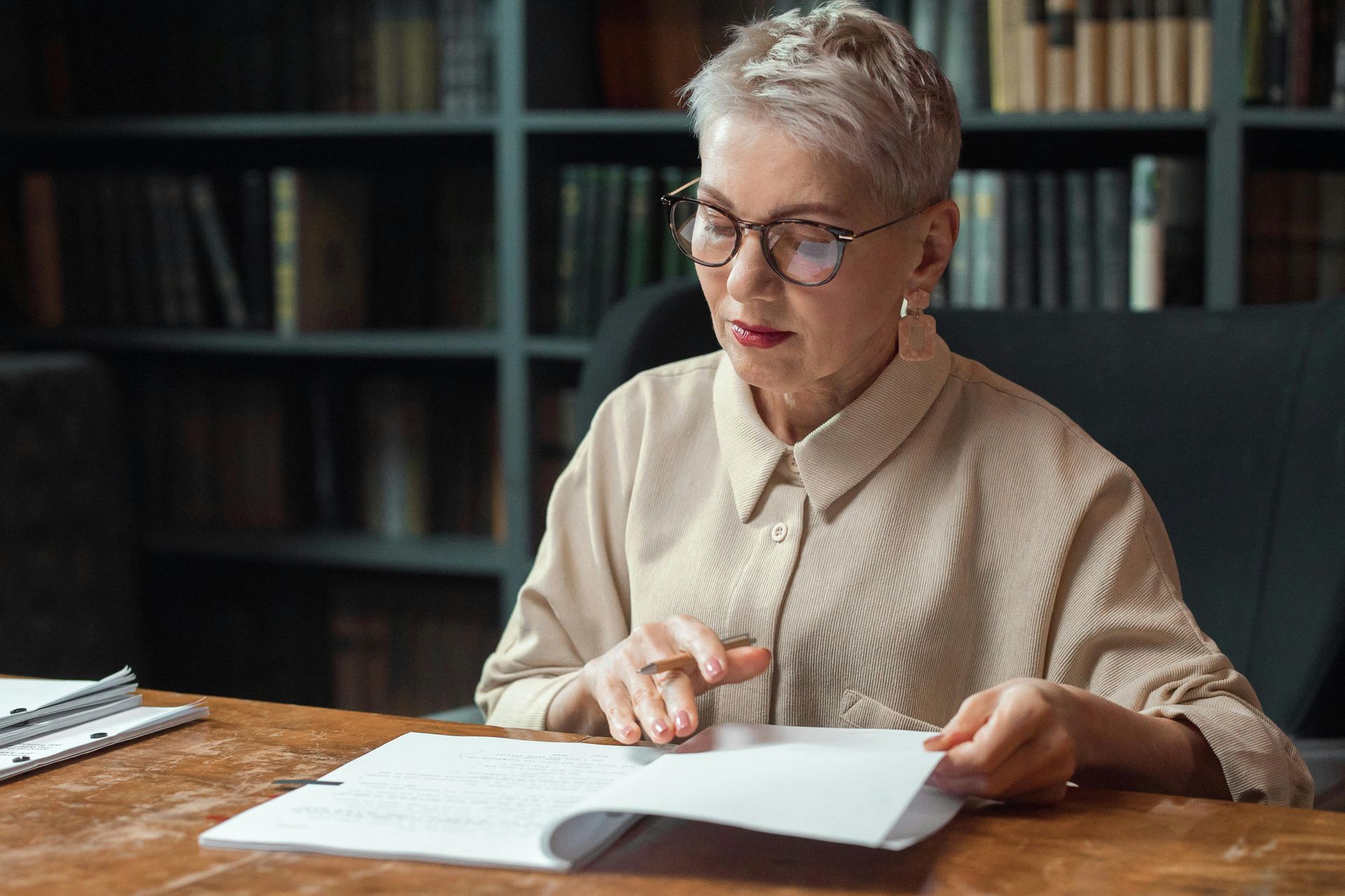 A woman is sitting at a desk in a library reading a book.