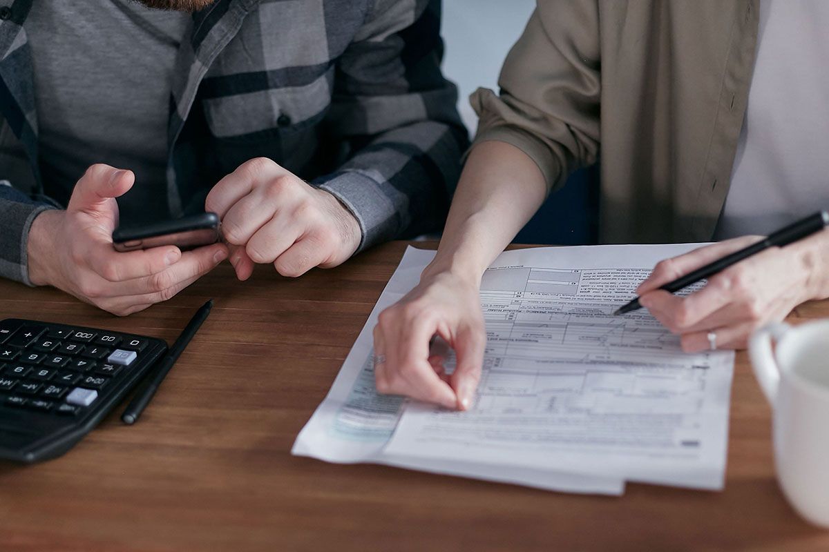 Two people reviewing paperwork at a wooden table, one pointing at documents while holding a pen.