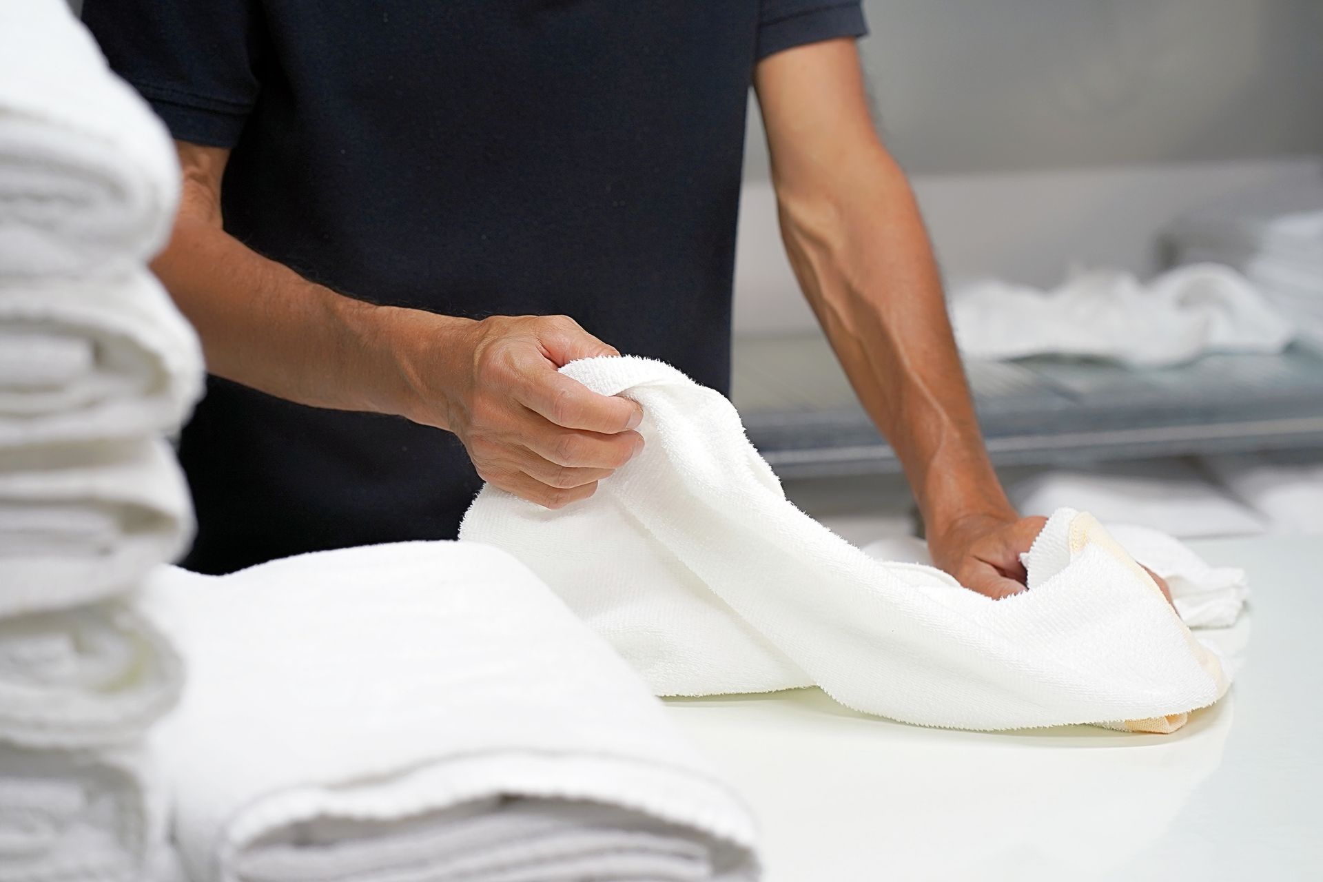 Hands of a Caucasian male laundry hotel worker folding a clean white towel.