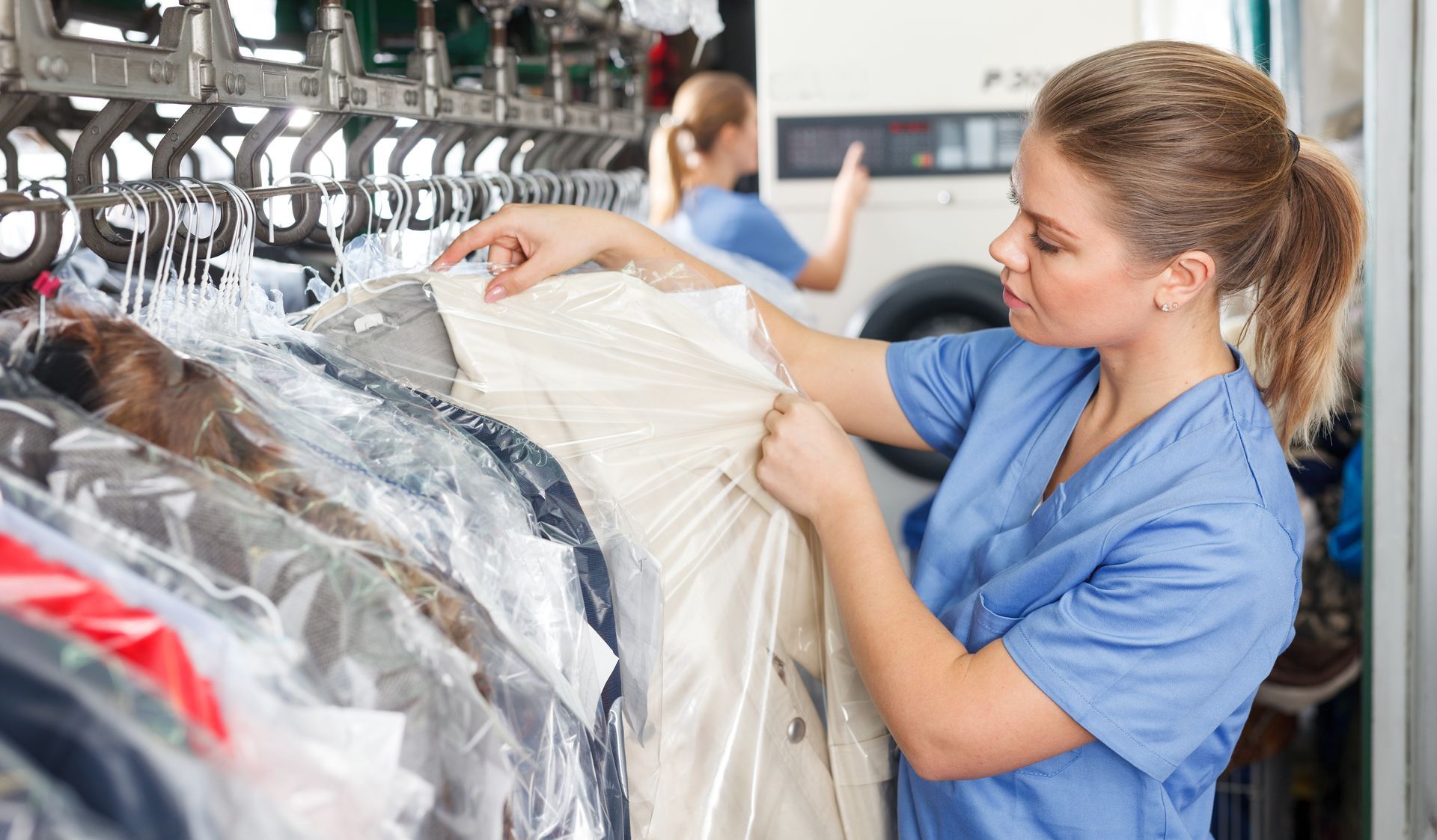 A female dry cleaner worker inspects the clothes on a rack.