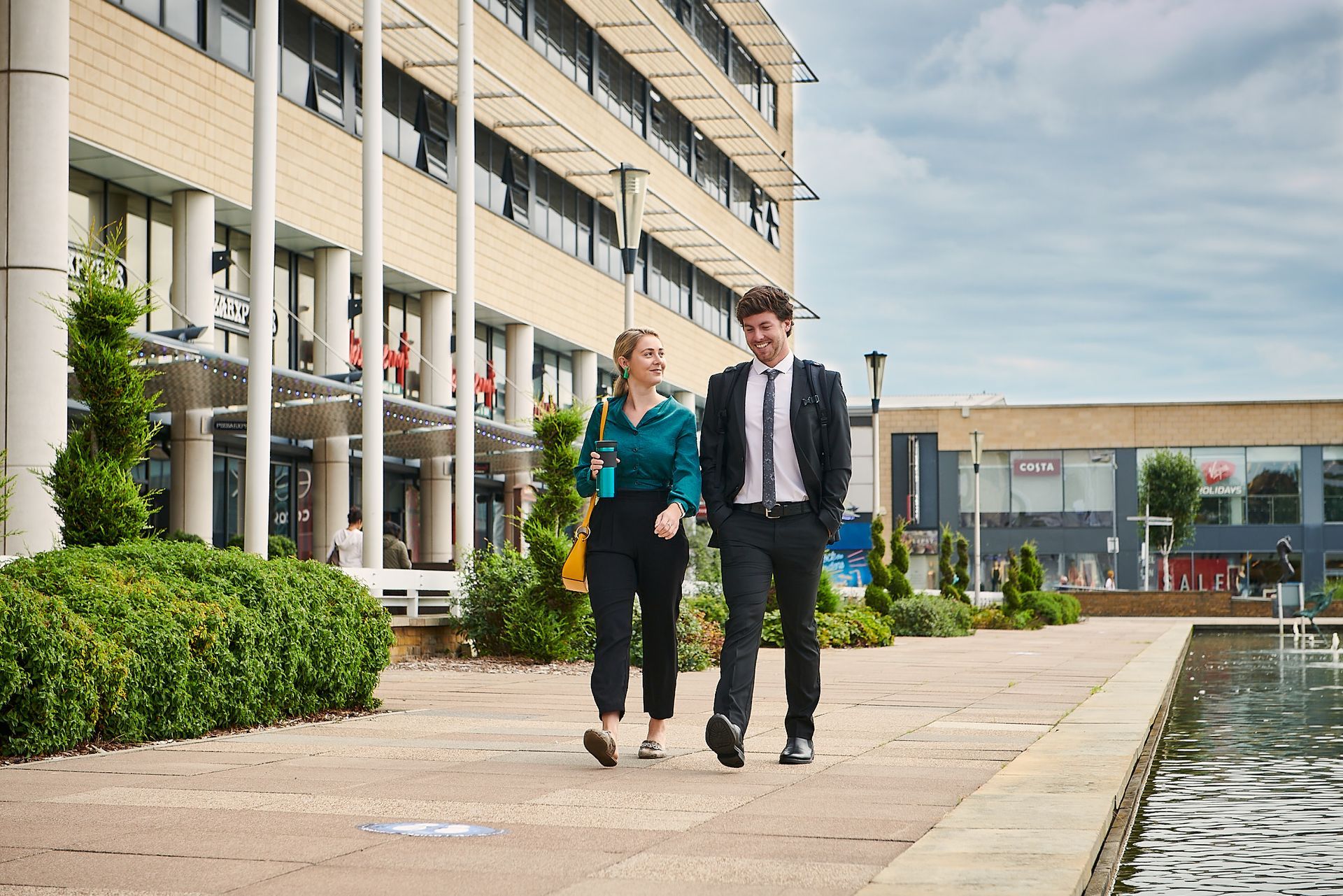 A man and a woman are walking down a sidewalk in front of a building.