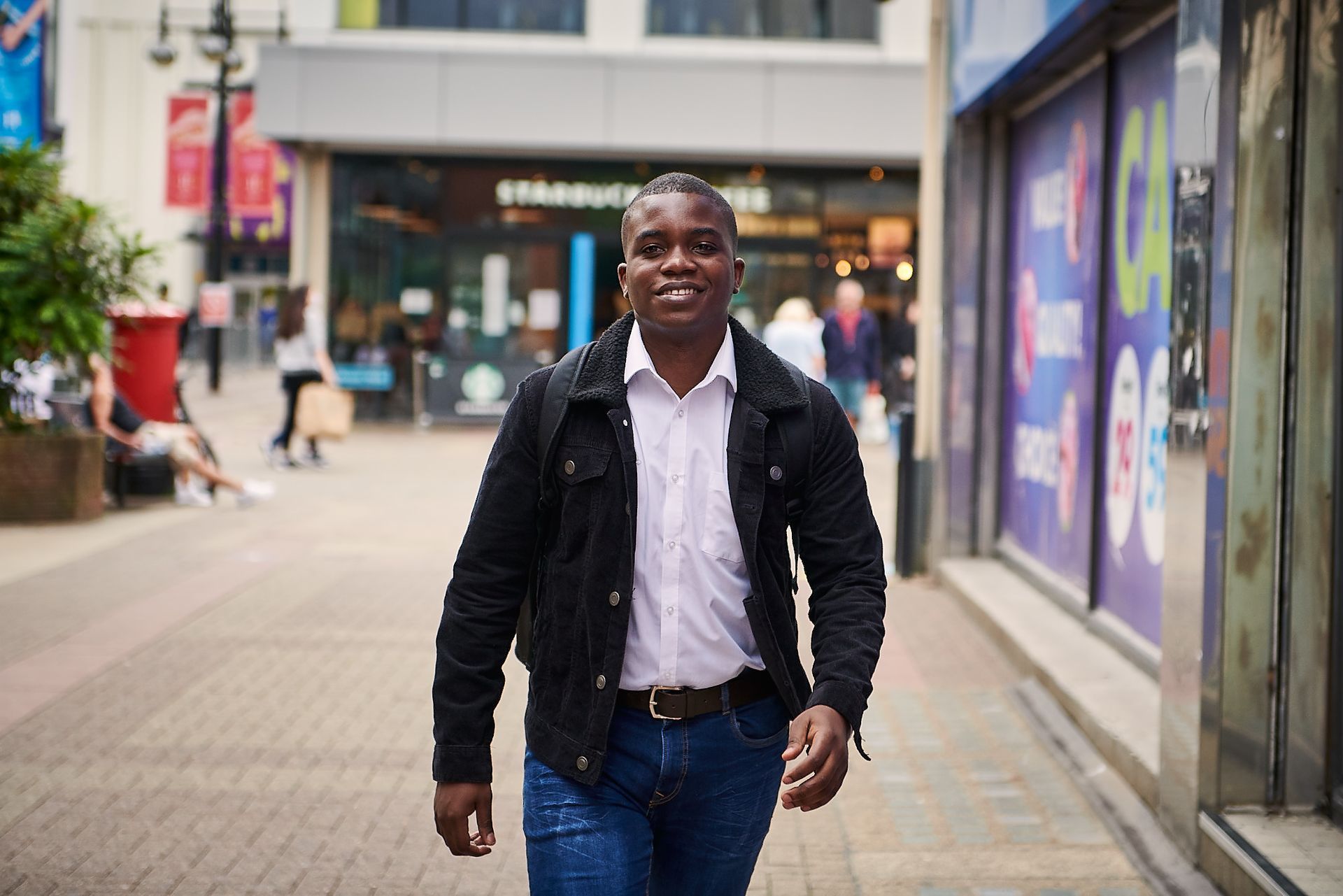A man in a black jacket is walking down a city street.