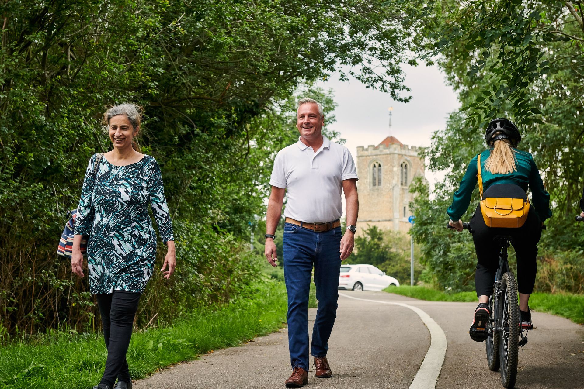 A man and two women are walking down a path next to a woman riding a bike.