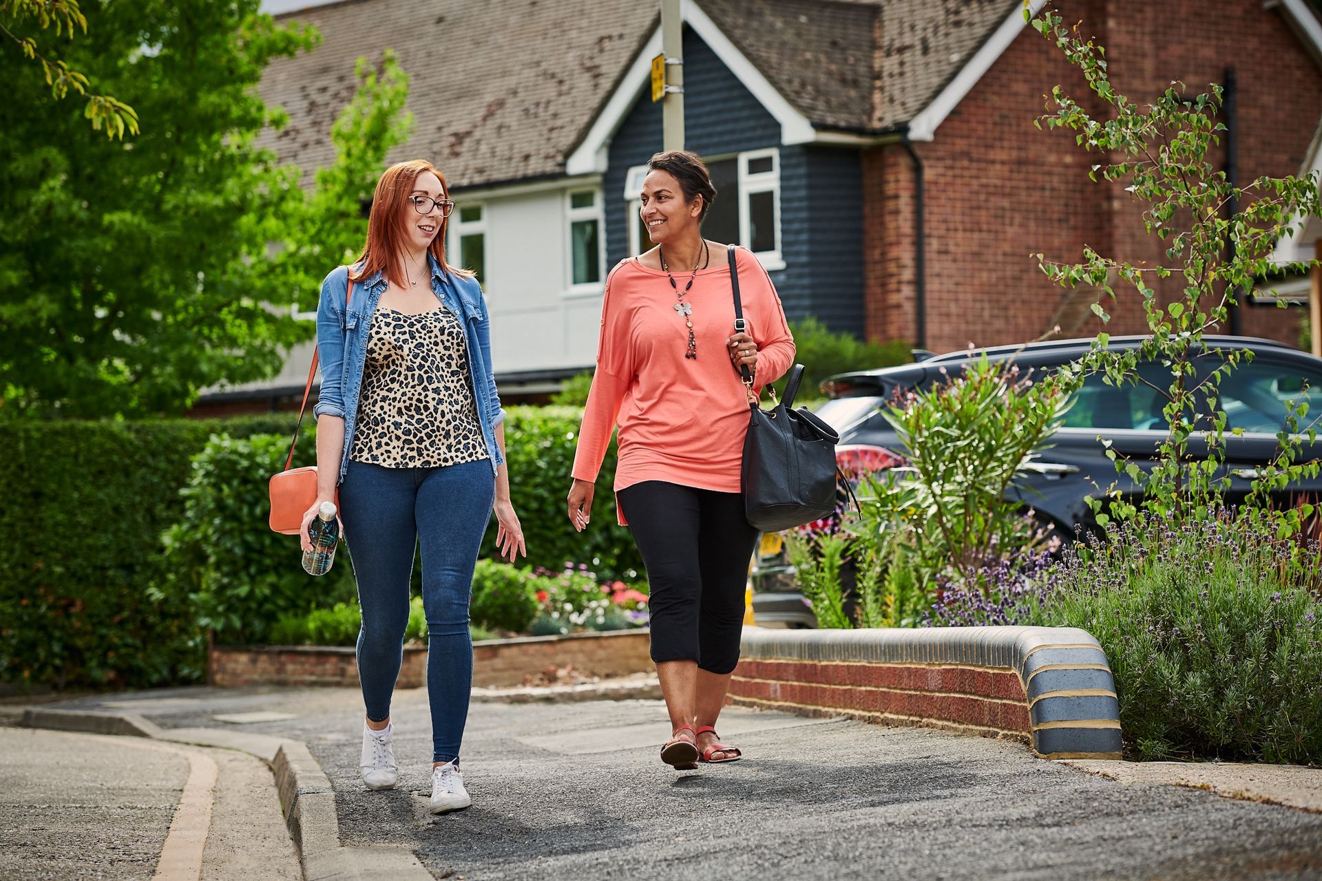 Two women are walking down a street in front of a house.