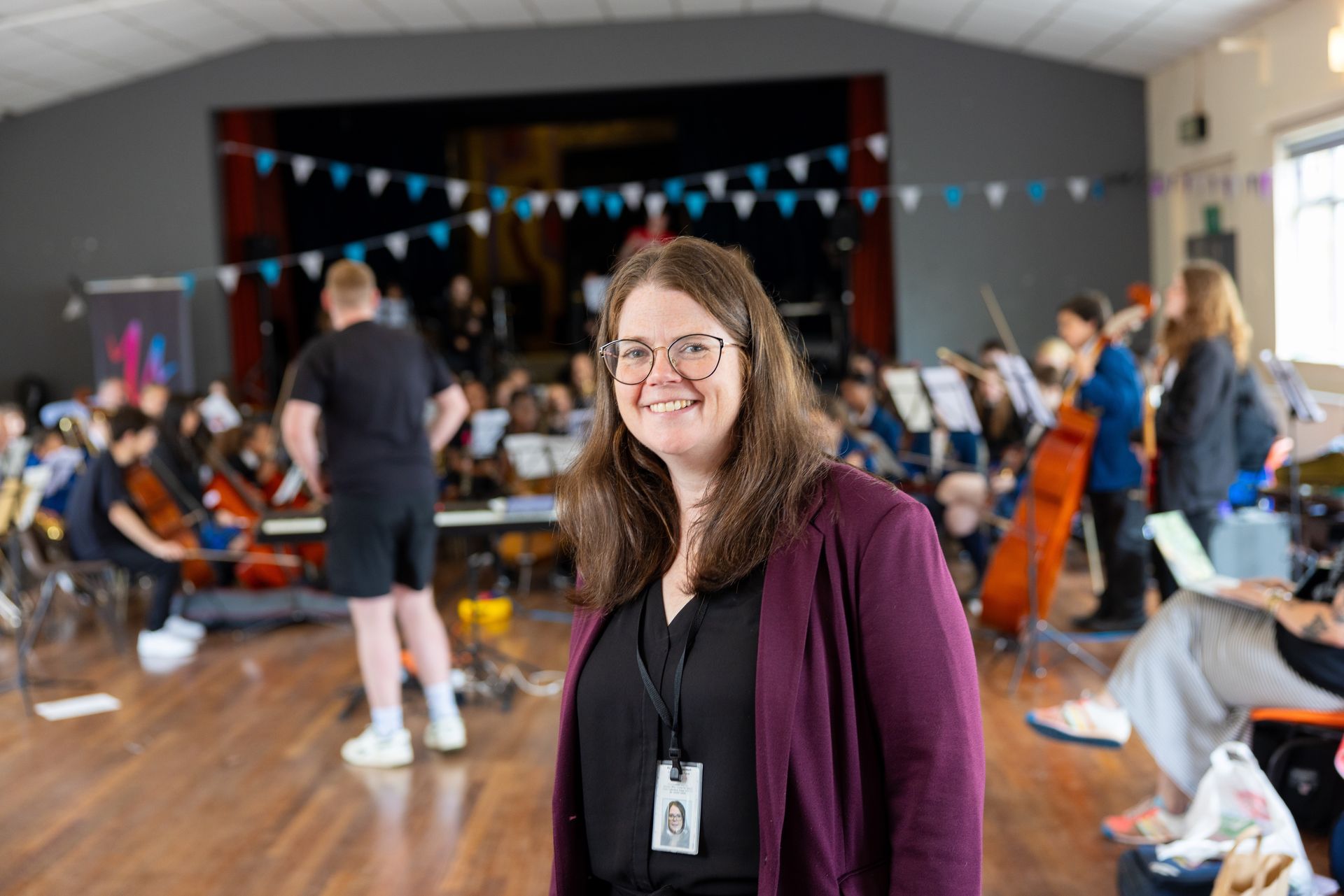 A woman is standing in front of an orchestra in a room.