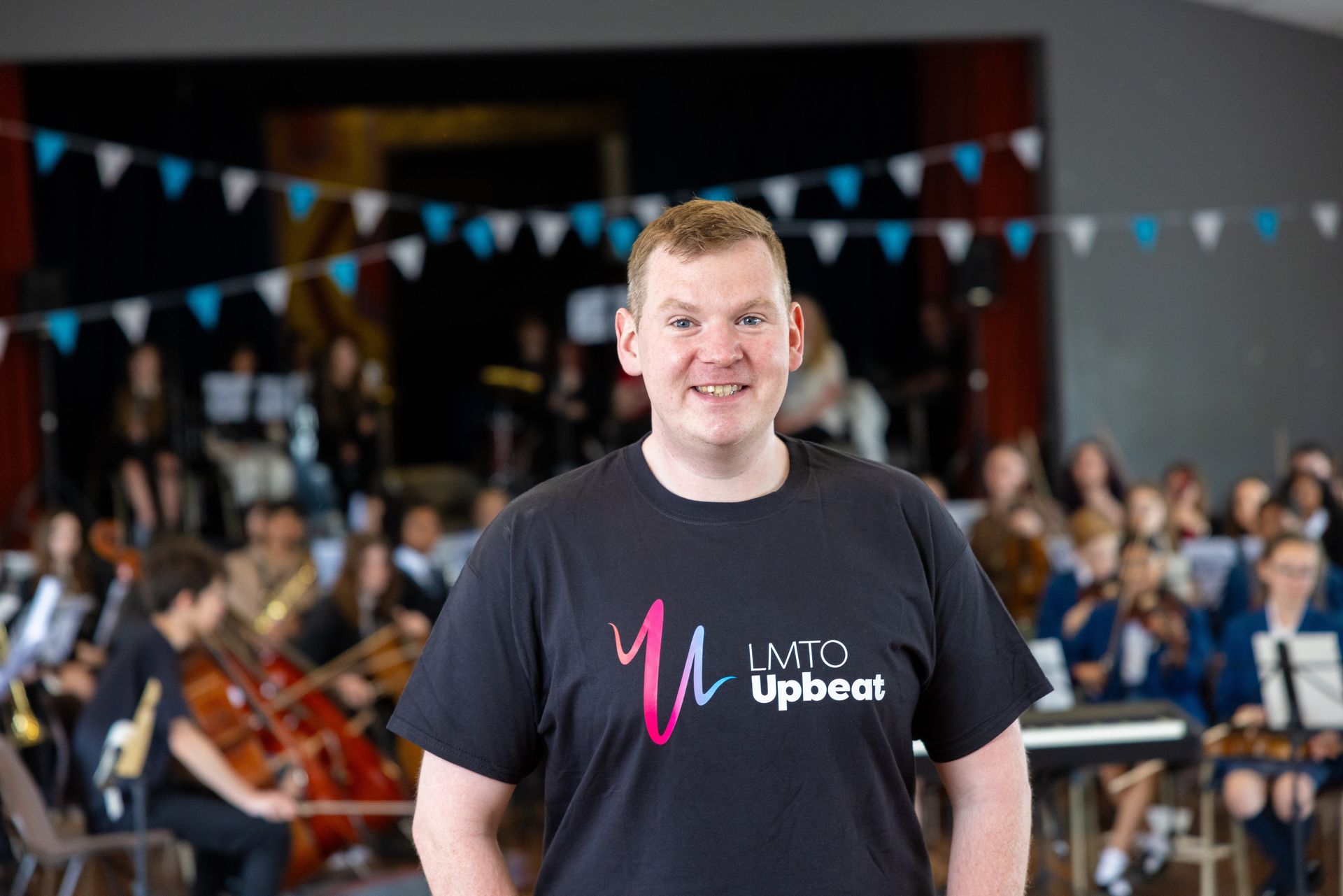 A man in a black shirt is standing in front of an orchestra.