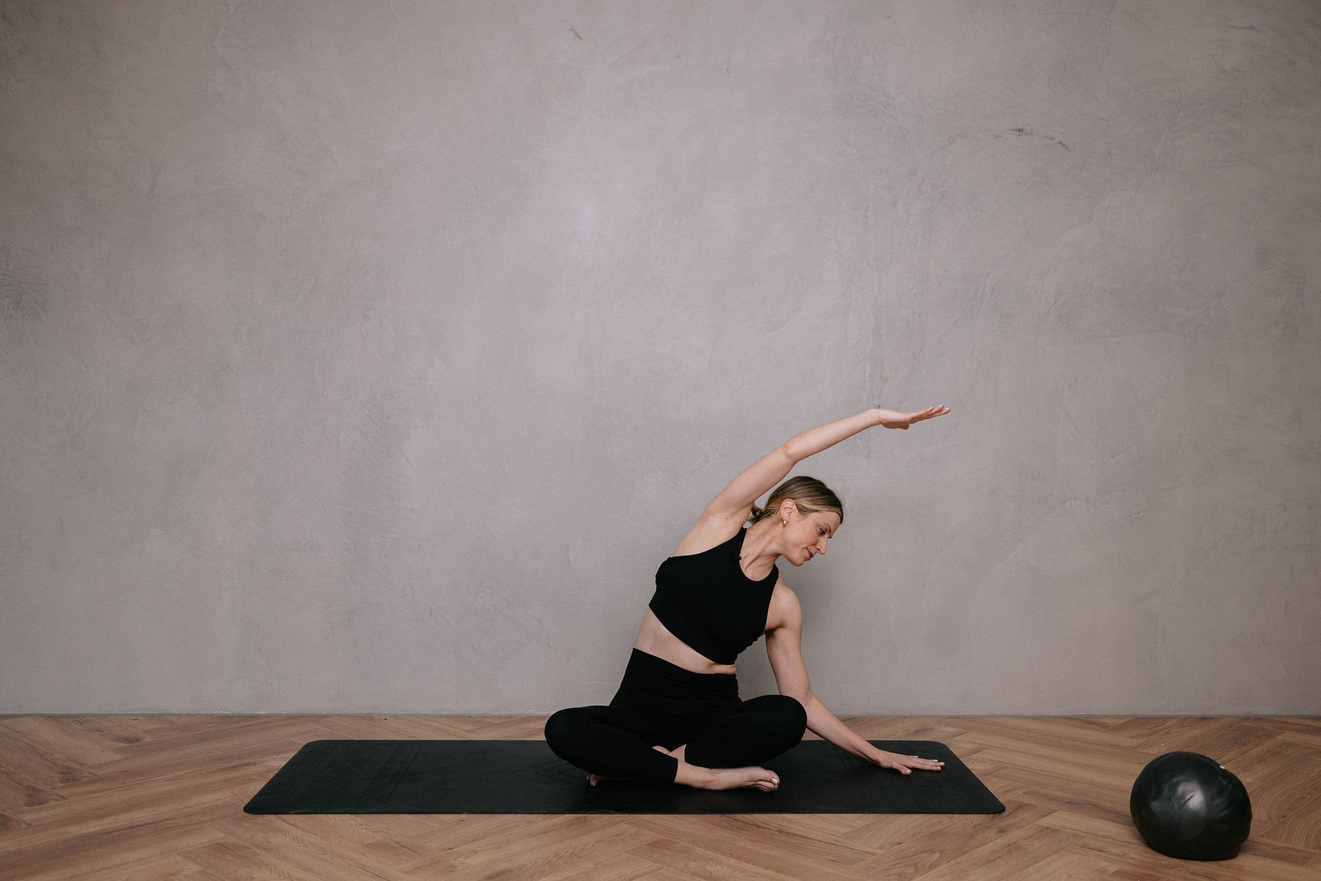 A woman is sitting on a yoga mat stretching her arms.