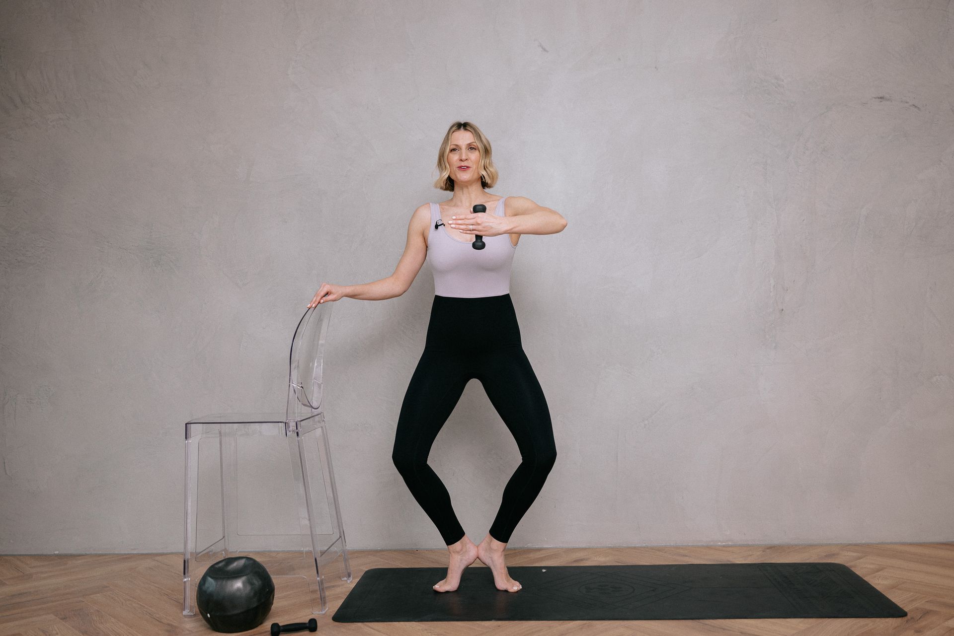 A woman is standing on a yoga mat next to a chair.