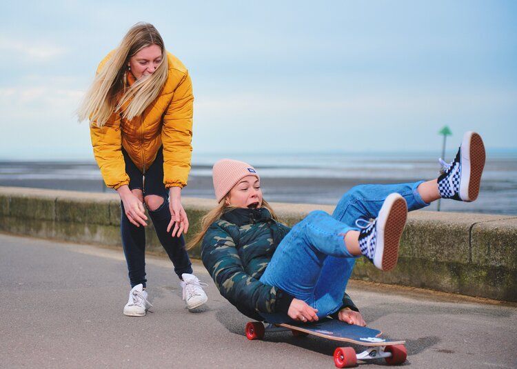 A woman is standing next to a girl on a skateboard.