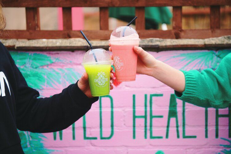 Two people are toasting with smoothies in front of a mural.