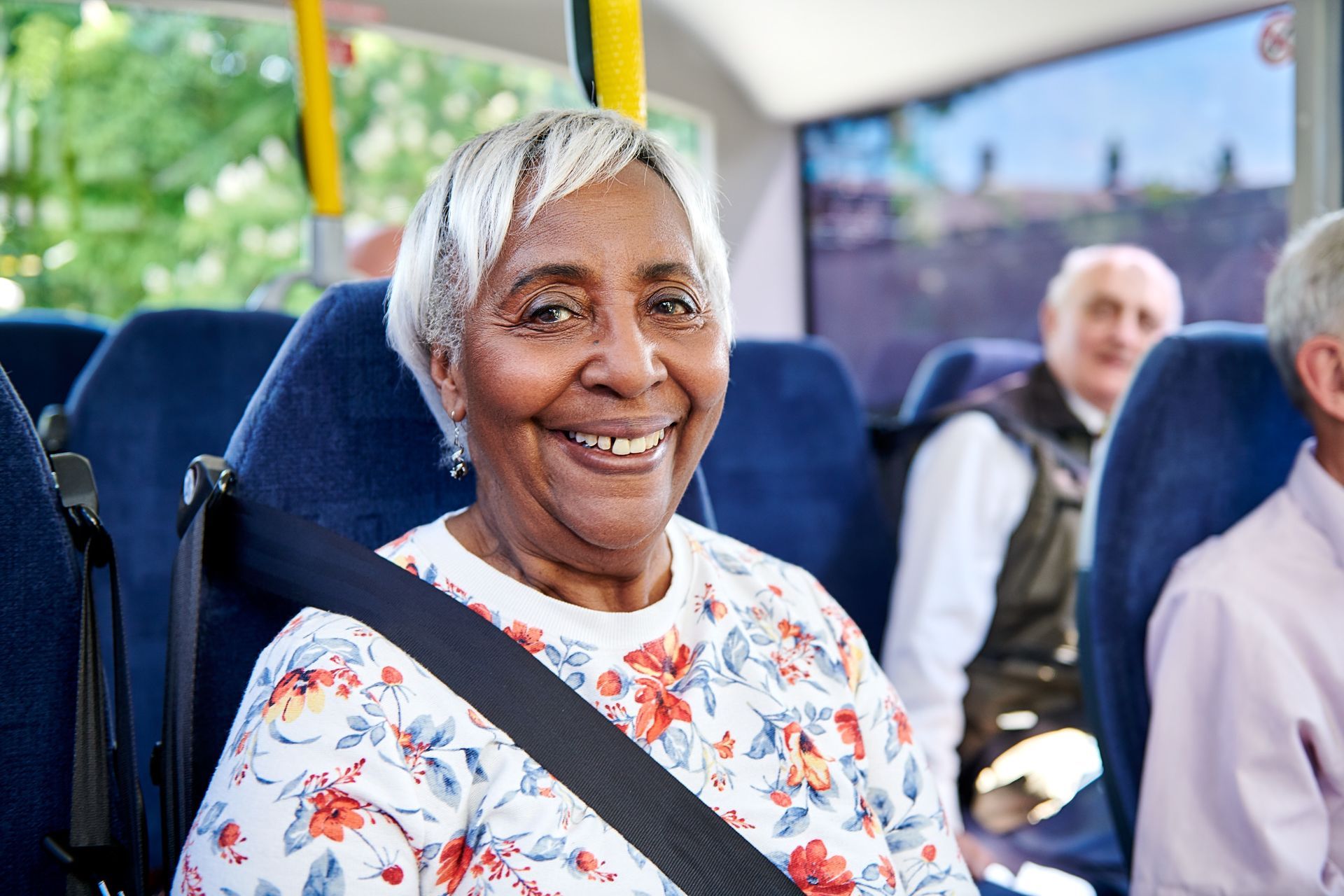 An elderly woman is smiling while sitting on a bus.