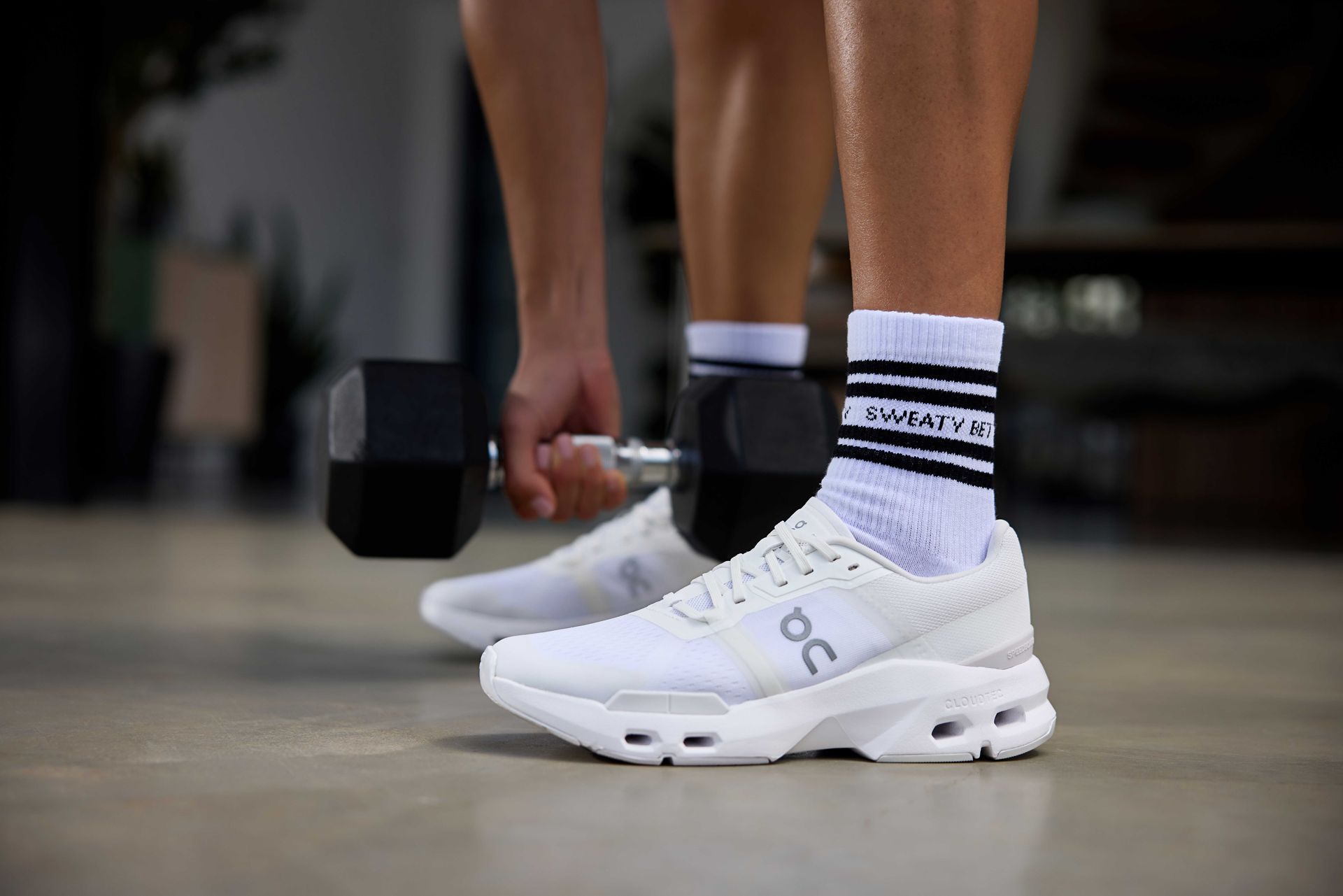 A person wearing white sneakers is lifting a dumbbell.