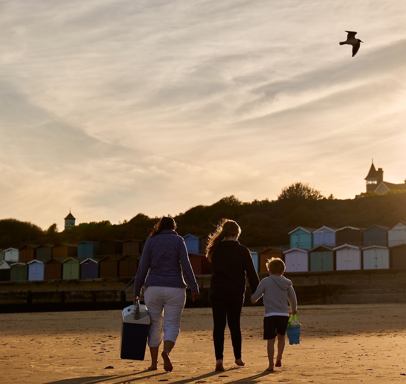 Three people walking on a beach with a bird flying in the sky