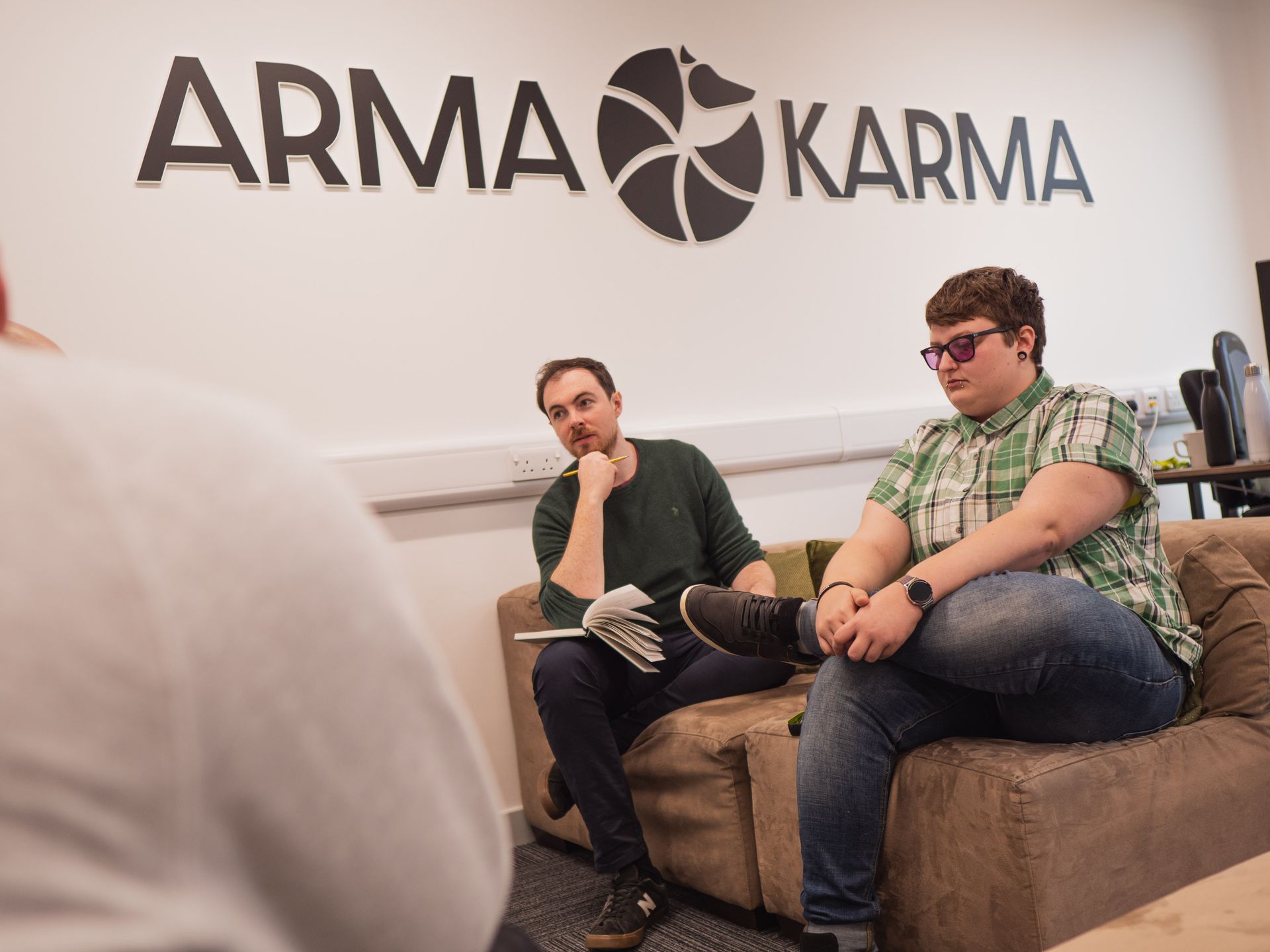 Two men are sitting on a couch under a sign that says arma karma.