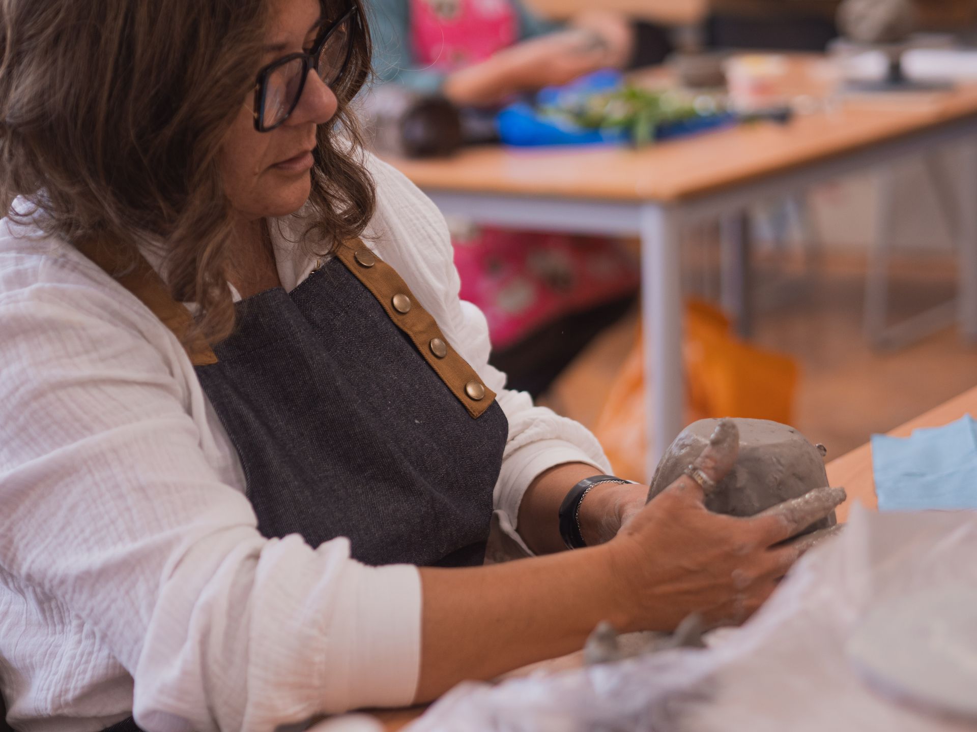 A woman is sitting at a table holding a piece of clay.