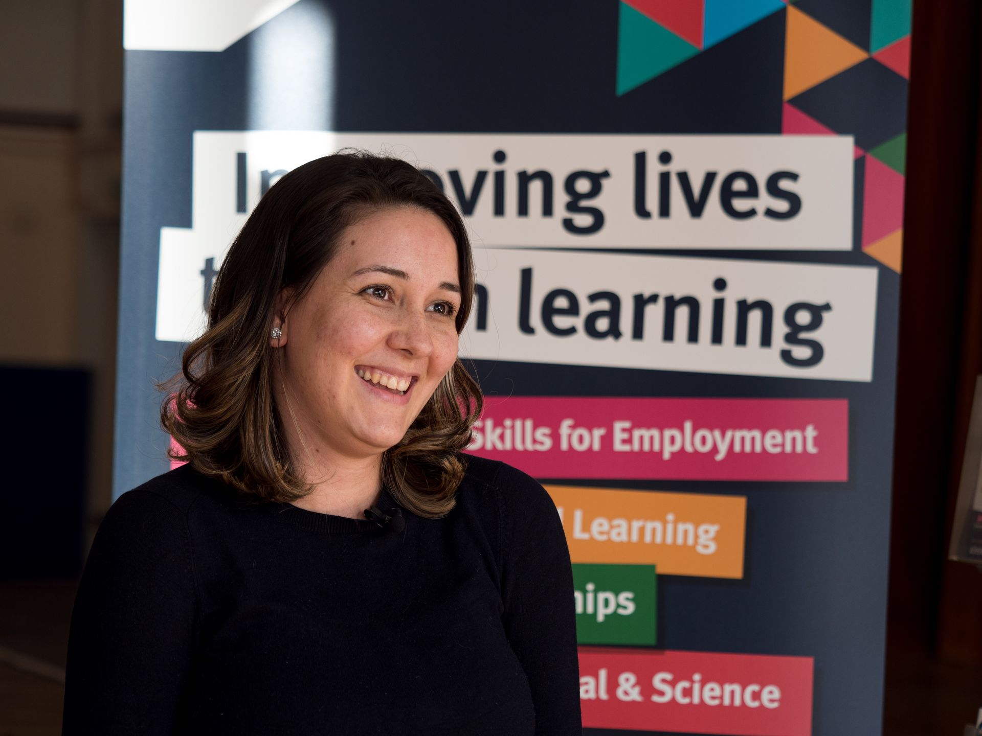 A woman is smiling in front of a sign that says leaving lives learning