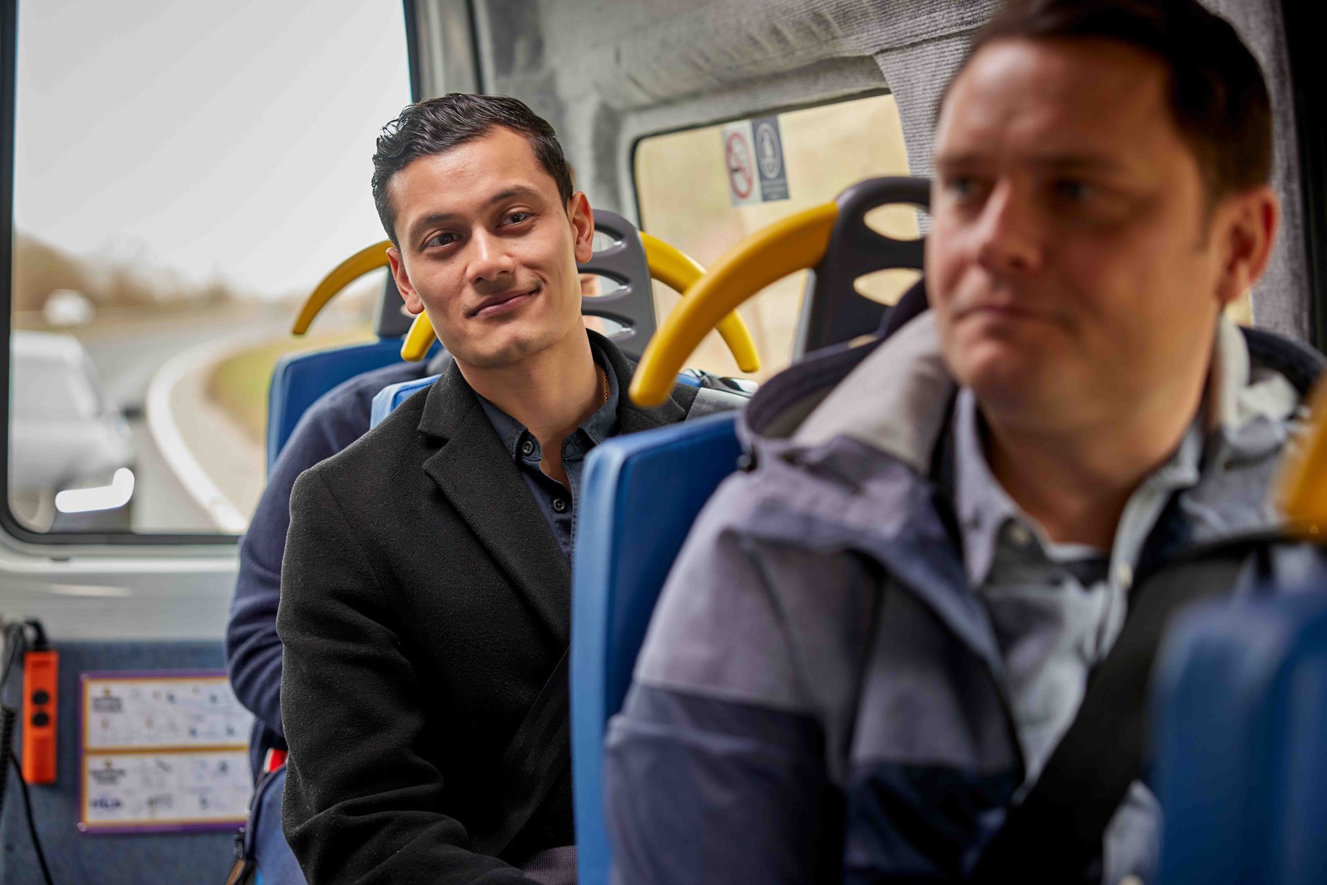 Two men are sitting on a bus looking out the window.